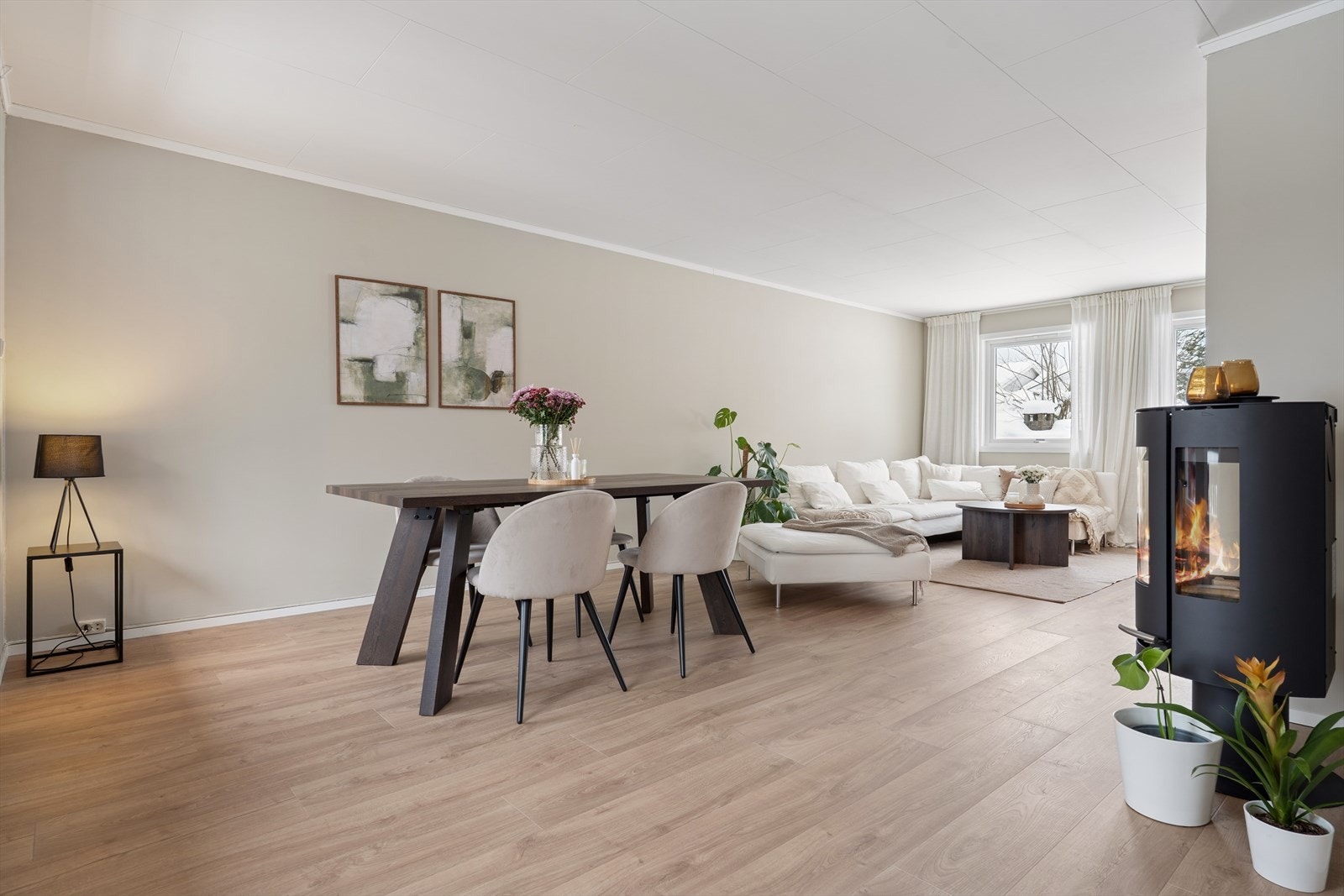 Den moderne peisovnen skaper en varm og stemningsfull atmosfære, og den åpne løsningen mot kjøkkenet gjør rommet ideelt for både hverdagsbruk og større sammenkomster Galleribilde