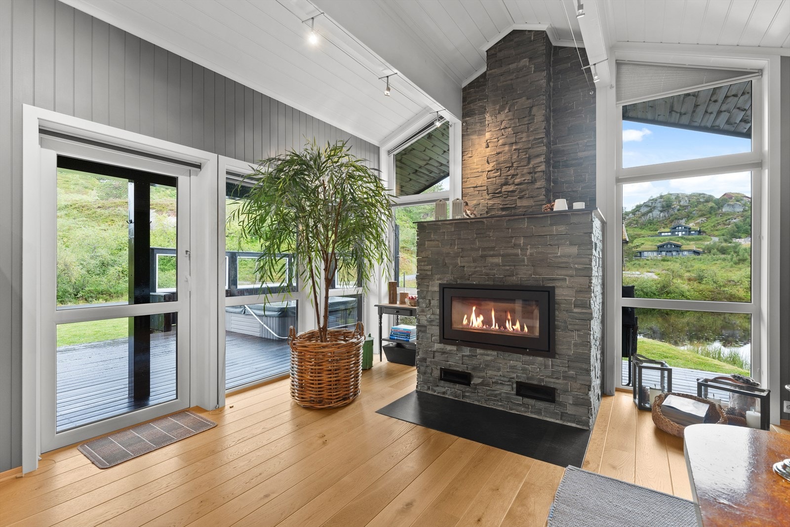 Peisen i stuen er som et smykke - pent innreammet at de store vindusflatene - her er det god kontakt med inne og uteområdene Galleribilde