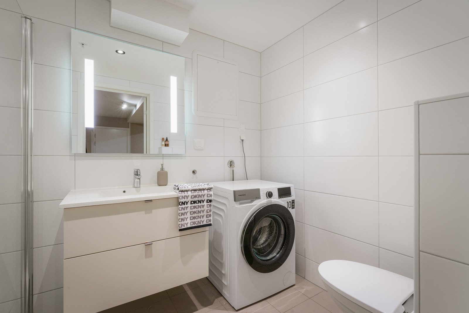 Store fliser gir et eksklusivt uttrykk. Badet er ellers innredet med servant med underskap, speil med integrert lys, innfellbart dusjhjørne i glass og vegghengt toalett. Galleribilde