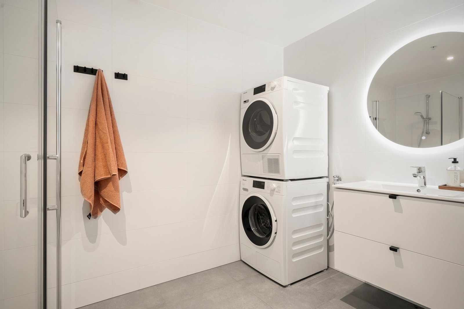 Moderne bad av god størrelse utstyrt med dusj med glassvegger, vegghengt toalett, servantseksjon med skuffer og speil med integrert belysning. Galleribilde