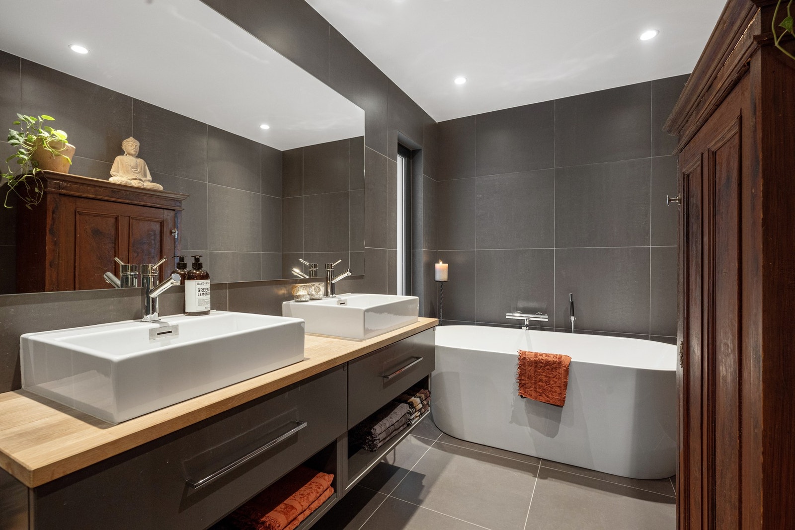 Badet fremstår moderne og eksklusivt med store fliser i rolige, mørke naturtoner. Galleribilde