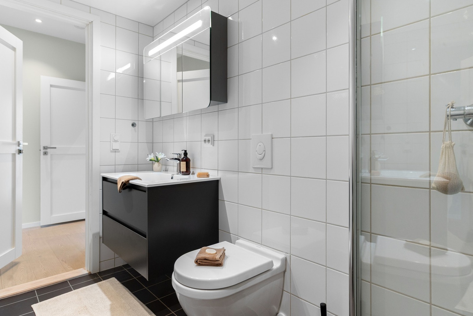 Badet er innredet med vegghengt toalett, servant med innredning, speilskap og dusjhjørne. Galleribilde