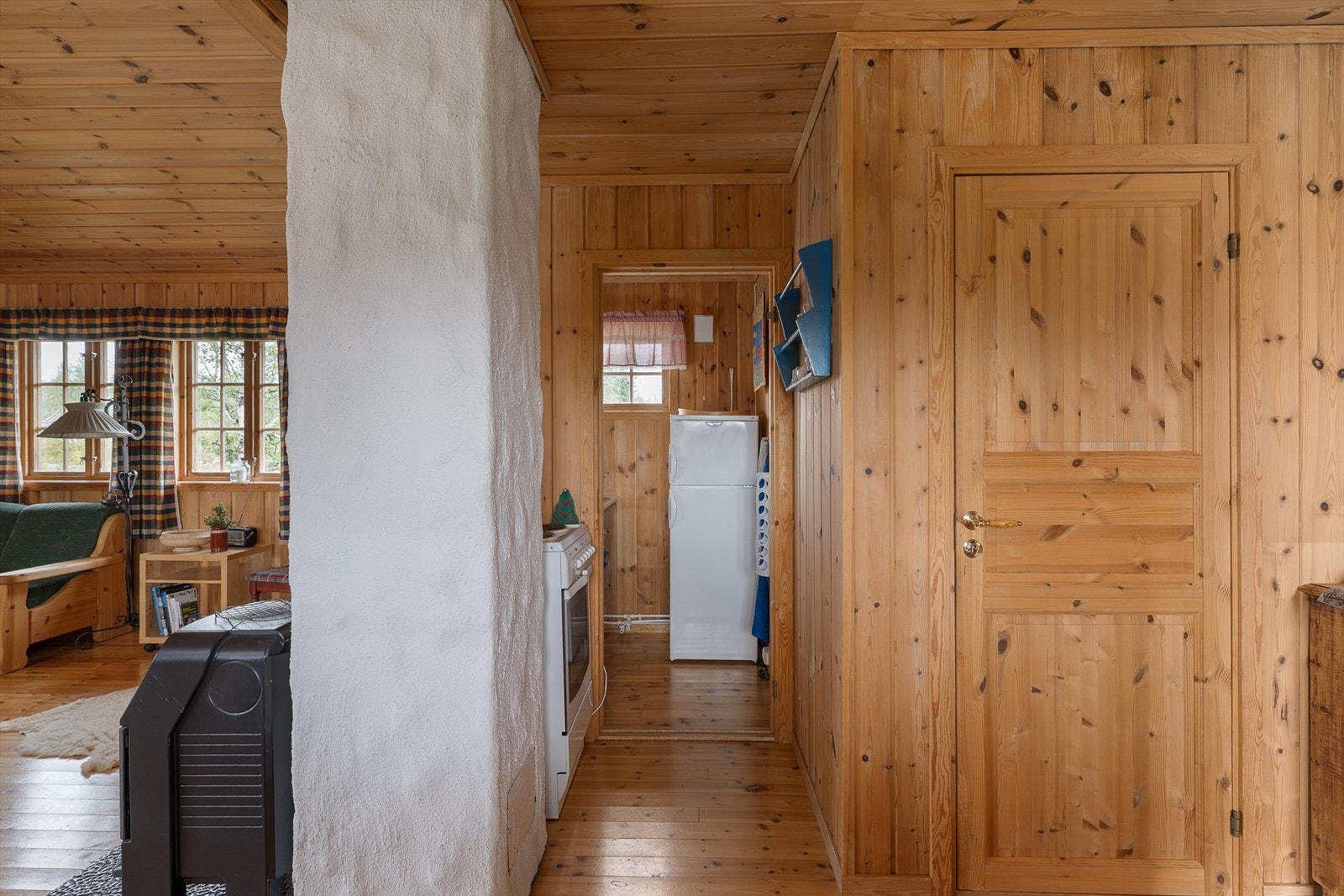 Komfyr og kjøleskap er plassert på andre siden av kjøkkeninnredningen, bak pipa. Galleribilde