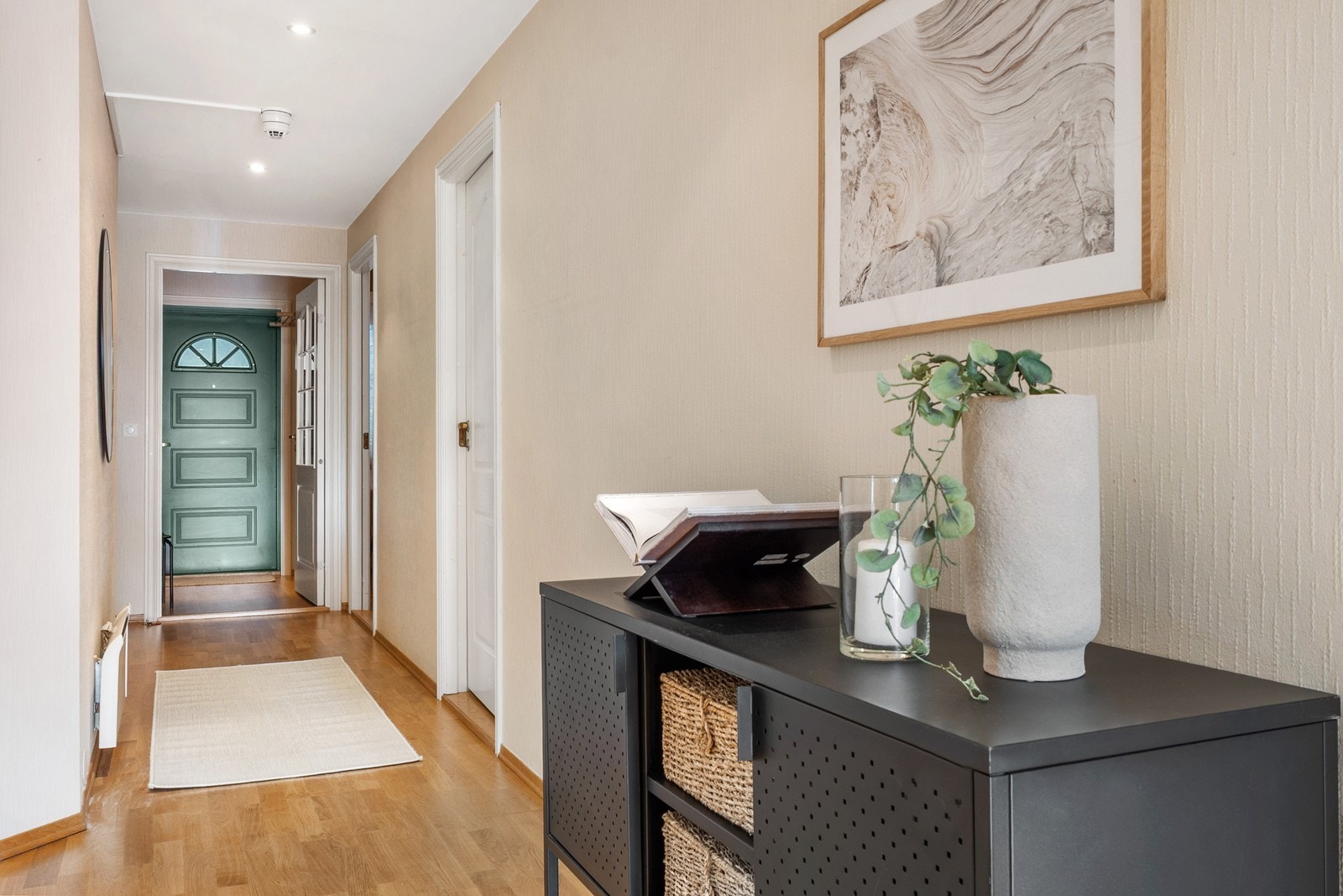 Leiligheten har et innbydende inngangsparti med adkomst fra svalgang. Inngangsdøren er i mørkgrønn utførelse og innenfor finner du et pent vindfang med lysmalte vegger og parkett på gulv. Galleribilde