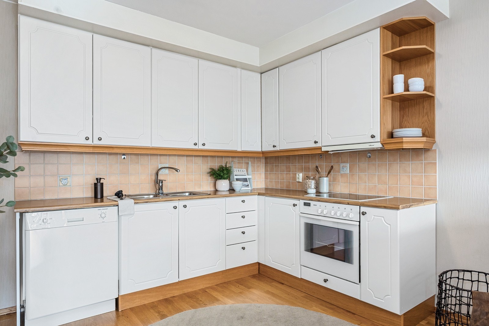 Kjøkkenet er plassert innerst i rommet og er funksjonelt innredet med skapfronter i malte, profilerte fronter, laminert benkeplate og fliser på vegg over benk. Galleribilde