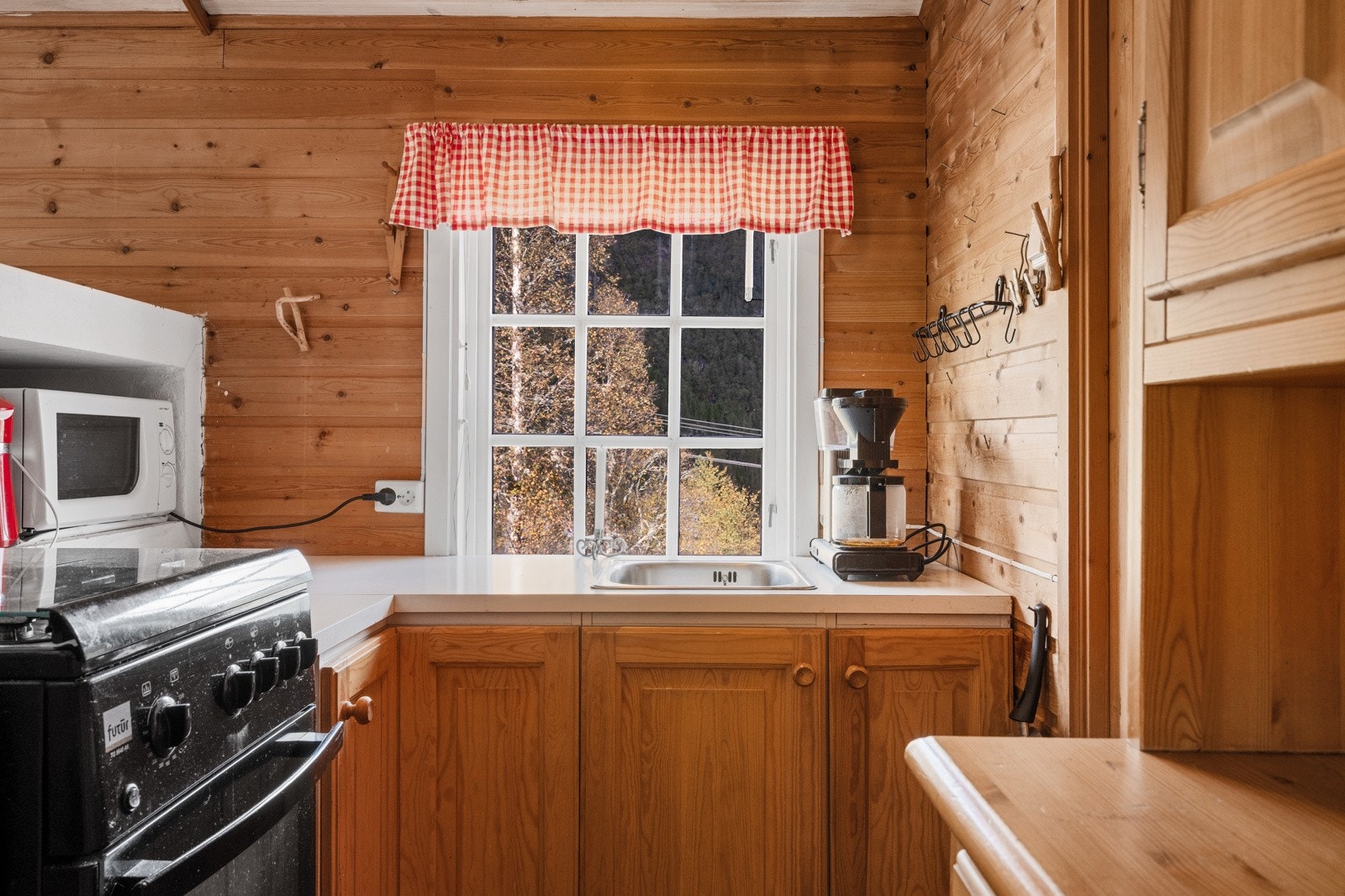 Et enkelt kjøkken med innredning i treverk, benkeplate med nedfelt stålvask og frittstående gasskomfyr. Galleribilde