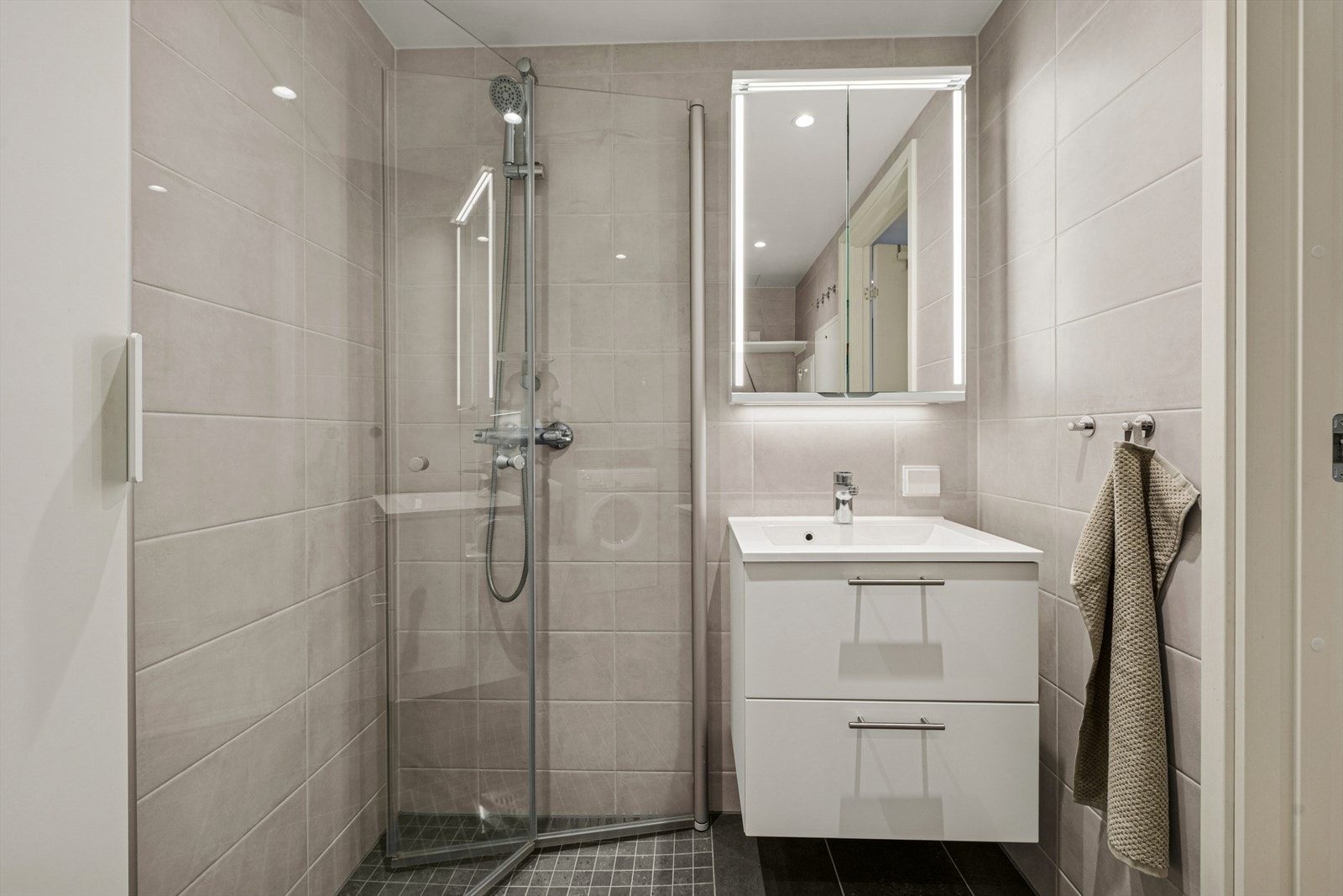 Baderommet er innredet med innfellbare dusjvegger, servant med skuffer, vegghengt wc, speil med ledlys og opplegg til vaskemaskin. Galleribilde