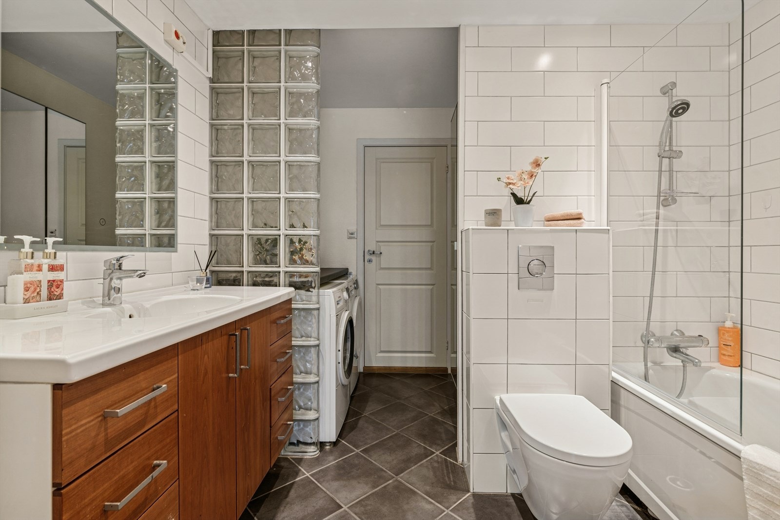 Pent og funksjonelt baderom med nyere innredning, vegghengt toalett og nisje til vask/tørk - praktisk plassert under benk. Dør inn til kjøkkenet. Galleribilde