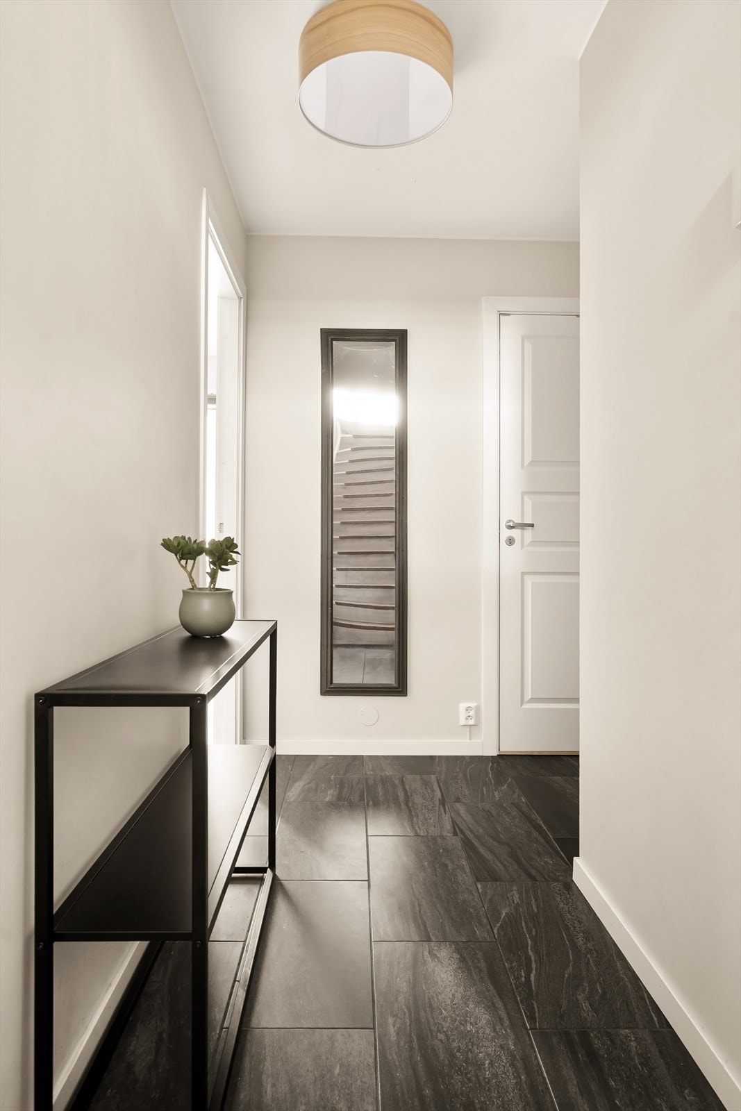 Gangen har mørke, slitesterke fliser på gulvet, og trappen leder opp til hovedetasjen. Galleribilde