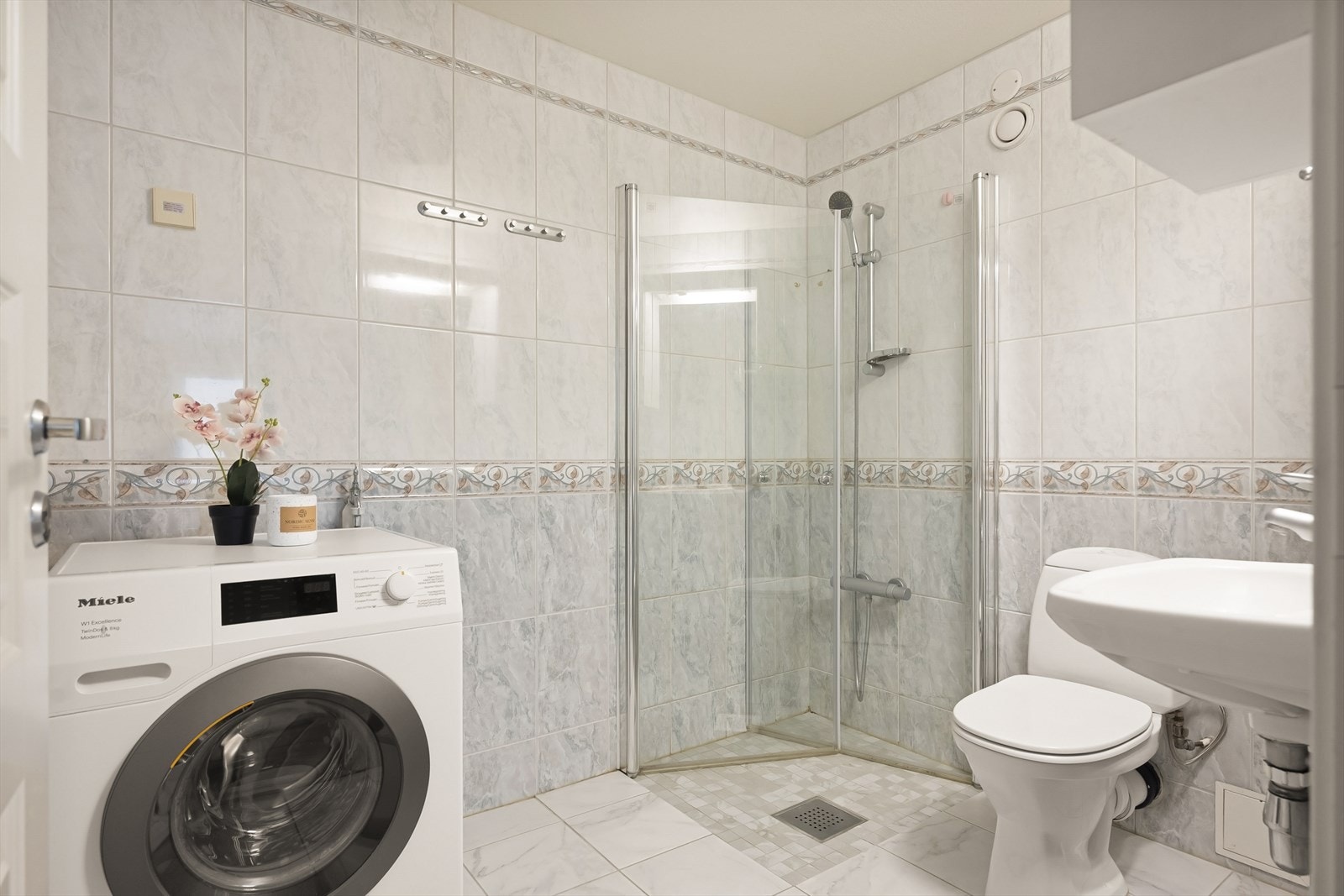 Badet har flislagte flater, gulvvarme og er utstyrt med toalett, servant, dusjhjørne og opplegg for vaskemaskin. Galleribilde