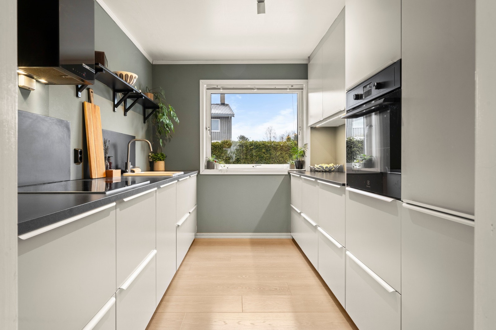 Kjøkkenet fremstår moderne og innbydende med stilrene, glatte fronter og en praktisk utforming som gir gode arbeidsflater samt rikelig med oppbevaringsplass. Den mørke laminatbenkeplaten skaper en elegant kontrast mot de lyse skapene, og vinduet slipper i Galleribilde