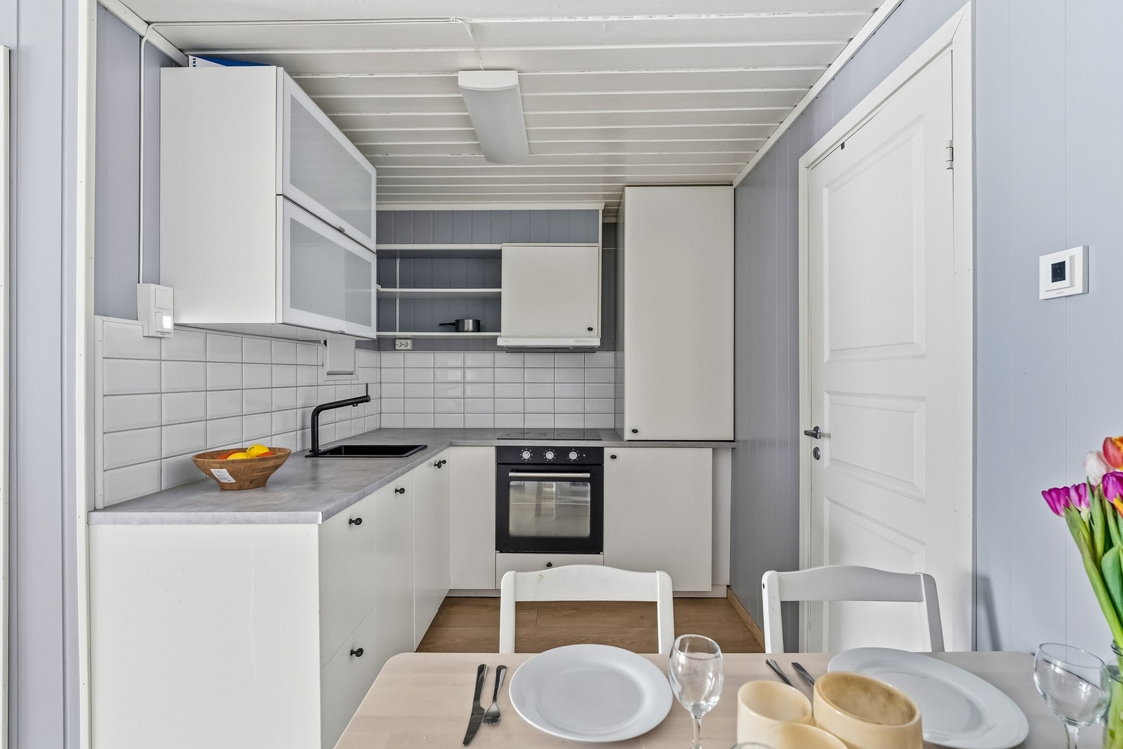 Innredningen har slette, hvite fronter, laminat benkeplate og nedfelt kum i mørk kompositt. Kjøkkenet er utstyrt med integrerte hvitevarer bestående av stekeovn, platetopp, oppvaskmaskin og kjøleskap. Galleribilde