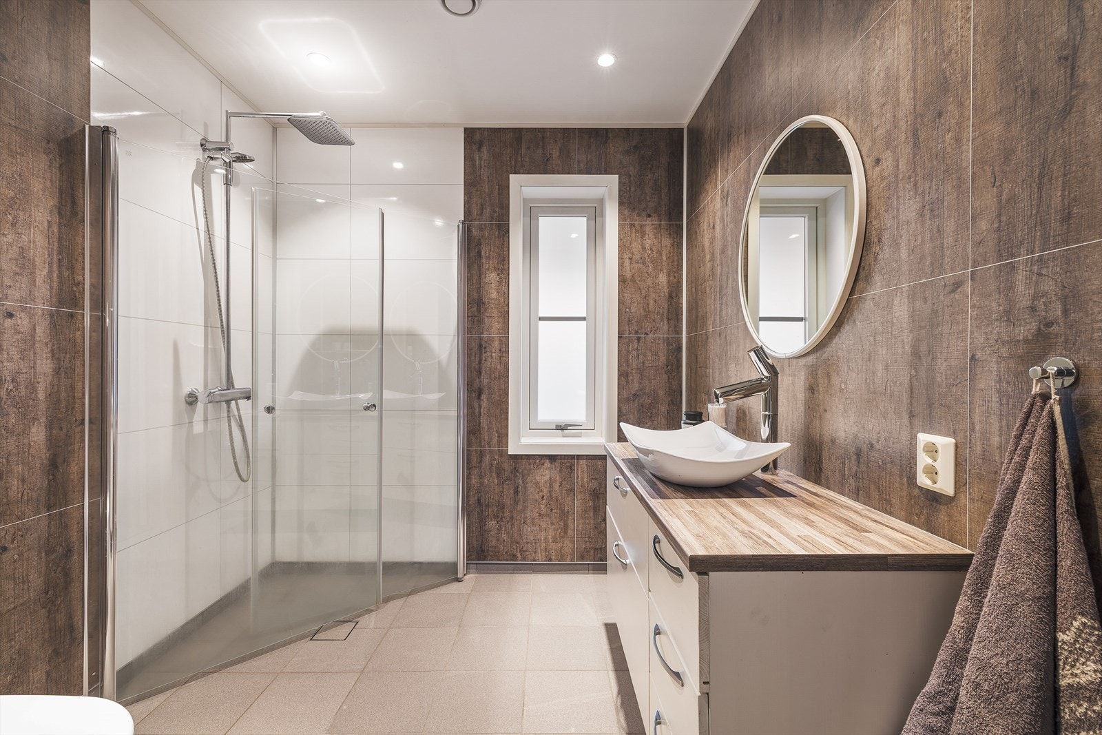 Badet i 1.etasje 4,7 m² og inneholder keramiske fliser på gulv, baderomsplater på vegger og malt platekledning i himling, med innfelte spotlights. Galleribilde