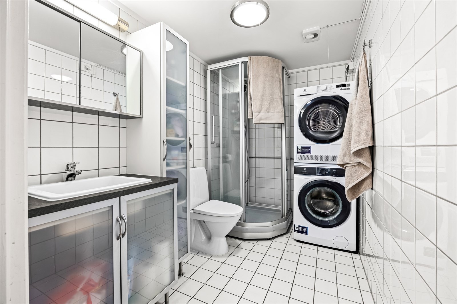 Badet er innredet med gulvstående klosett, baderomsinnredning med servant, speilskap og dusjkabinett. Galleribilde