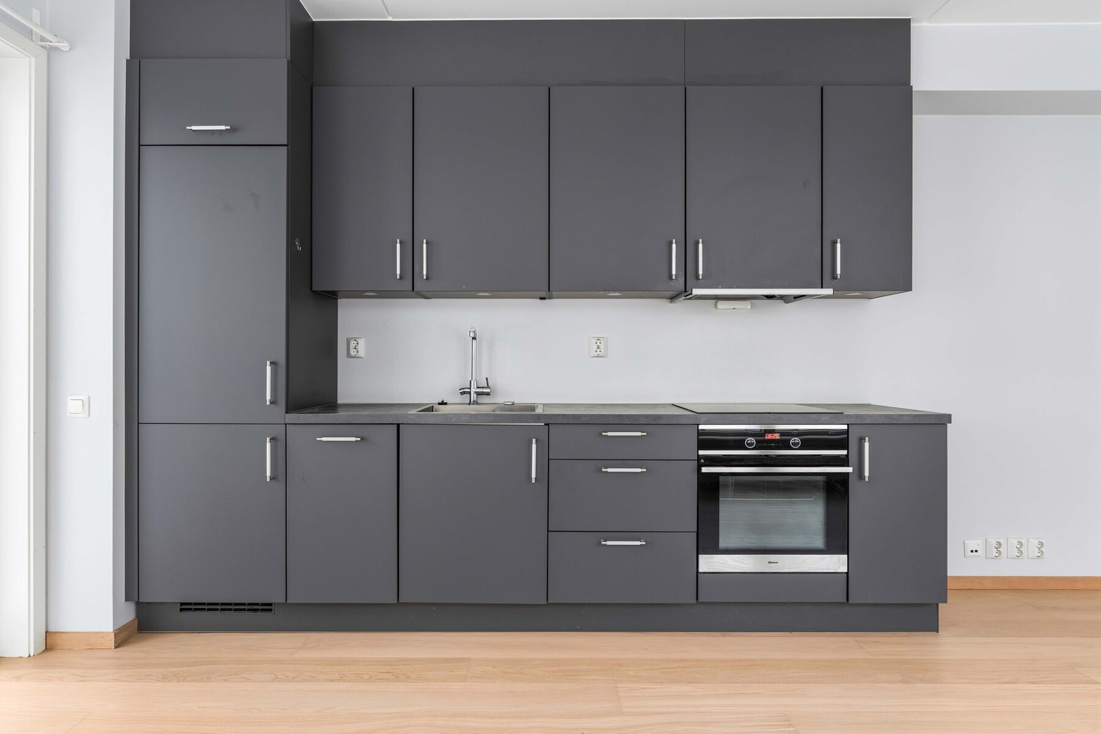 Kjøkkeninnredning består av glatte sorte fronter, benkeplate av laminat, oppvaskkum av stål, og integrerte hvitevarer Galleribilde