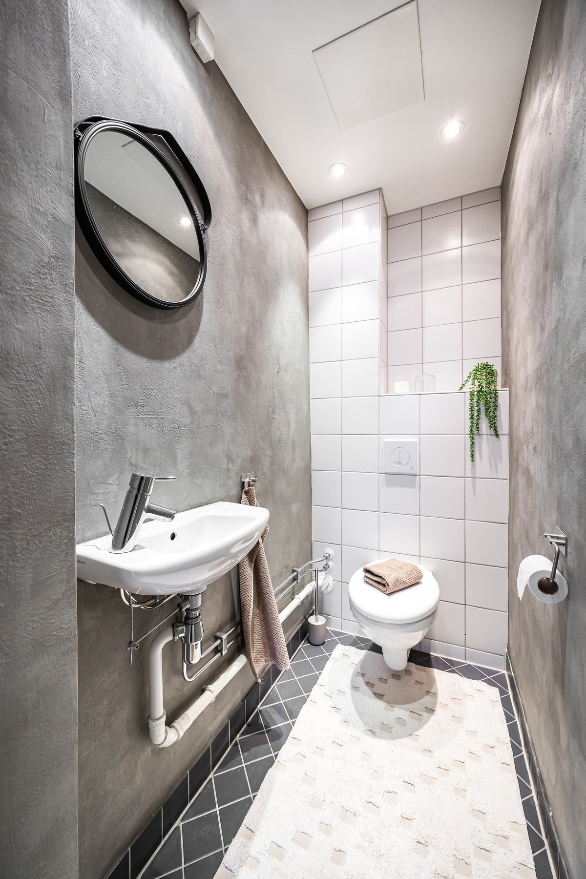 Toalettrom med flislagt gulv og varmekabler, veggflater delvis flislagt og delvis malt. Rommet har veggmontert servant med ett-greps armatur i krom, samt innebygget sisterne med vegghengt toalett. Galleribilde