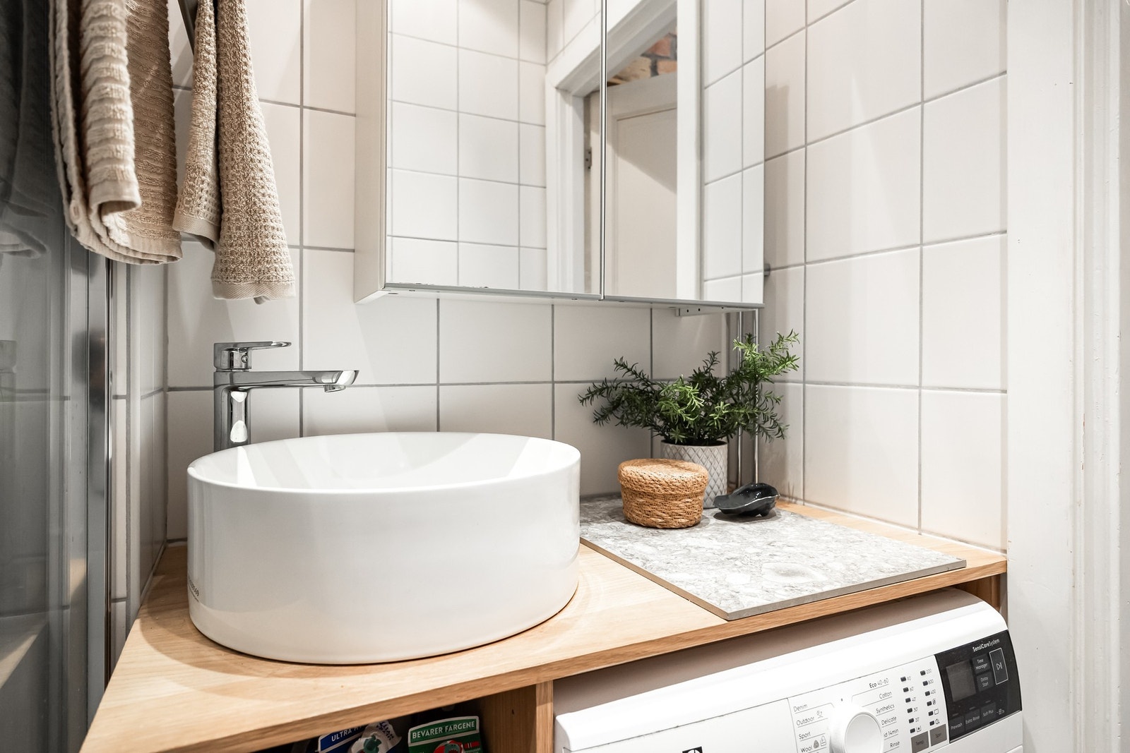 Badet har servantinnredning med utenpåliggende vask og ett-greps armatur i krom, opplegg for vaskemaskin, samt veggmontert speilskap. Galleribilde