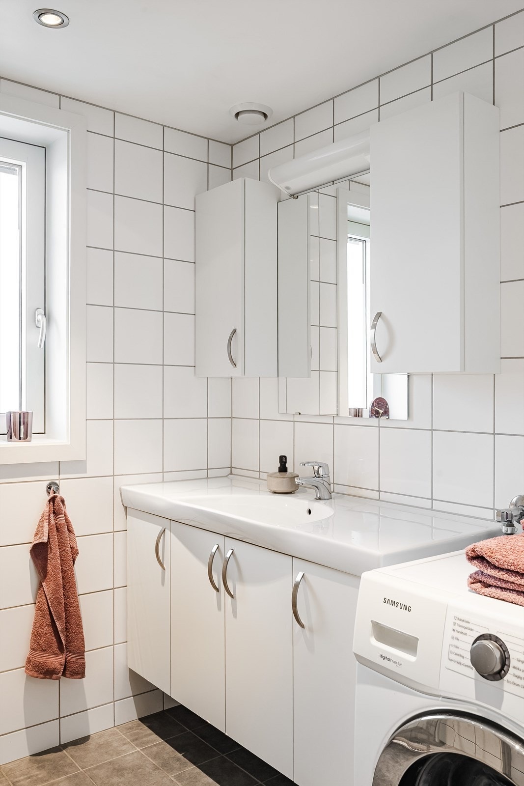 Baderommet er innredet med servant på innredning, dusjhjørne med glassdører, vegghengt toalett og opplegg for vaskemaskin. Galleribilde