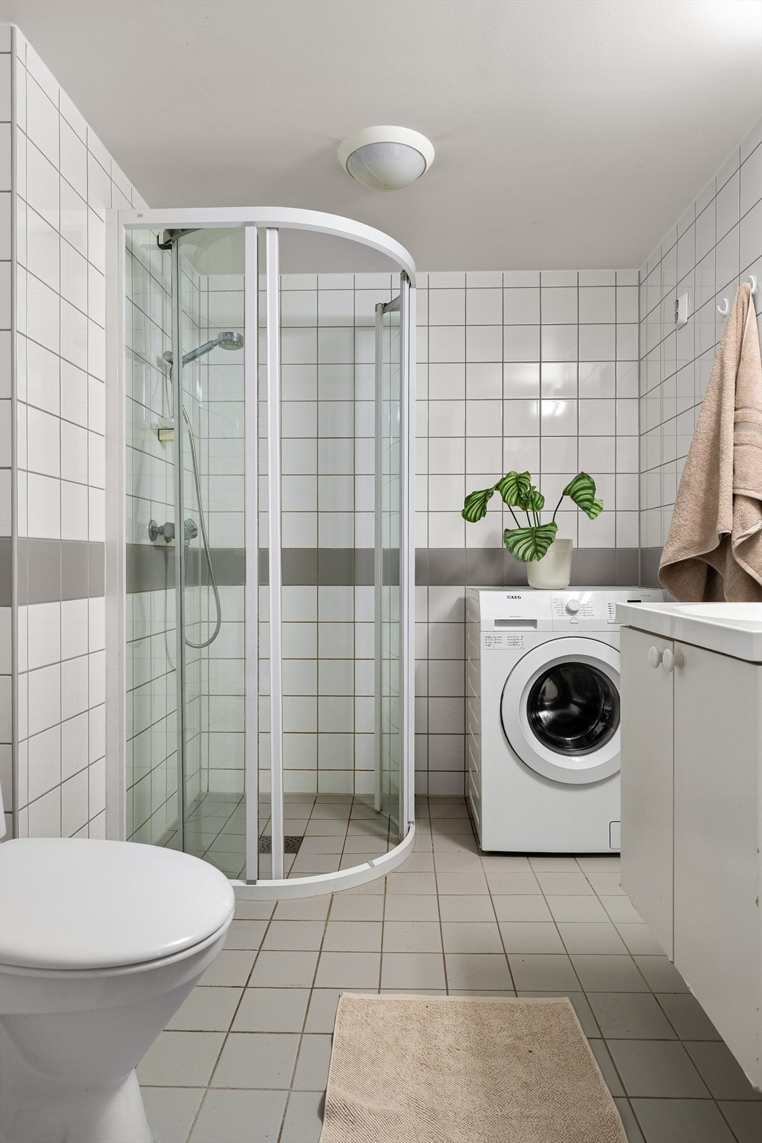 Badet er praktisk plassert ved entréen og er utstyrt med veggmontert dusjhjørne, servant med underskap, speil med belysning over, veggmontert wc samt opplegg for vaskemaskin. Galleribilde