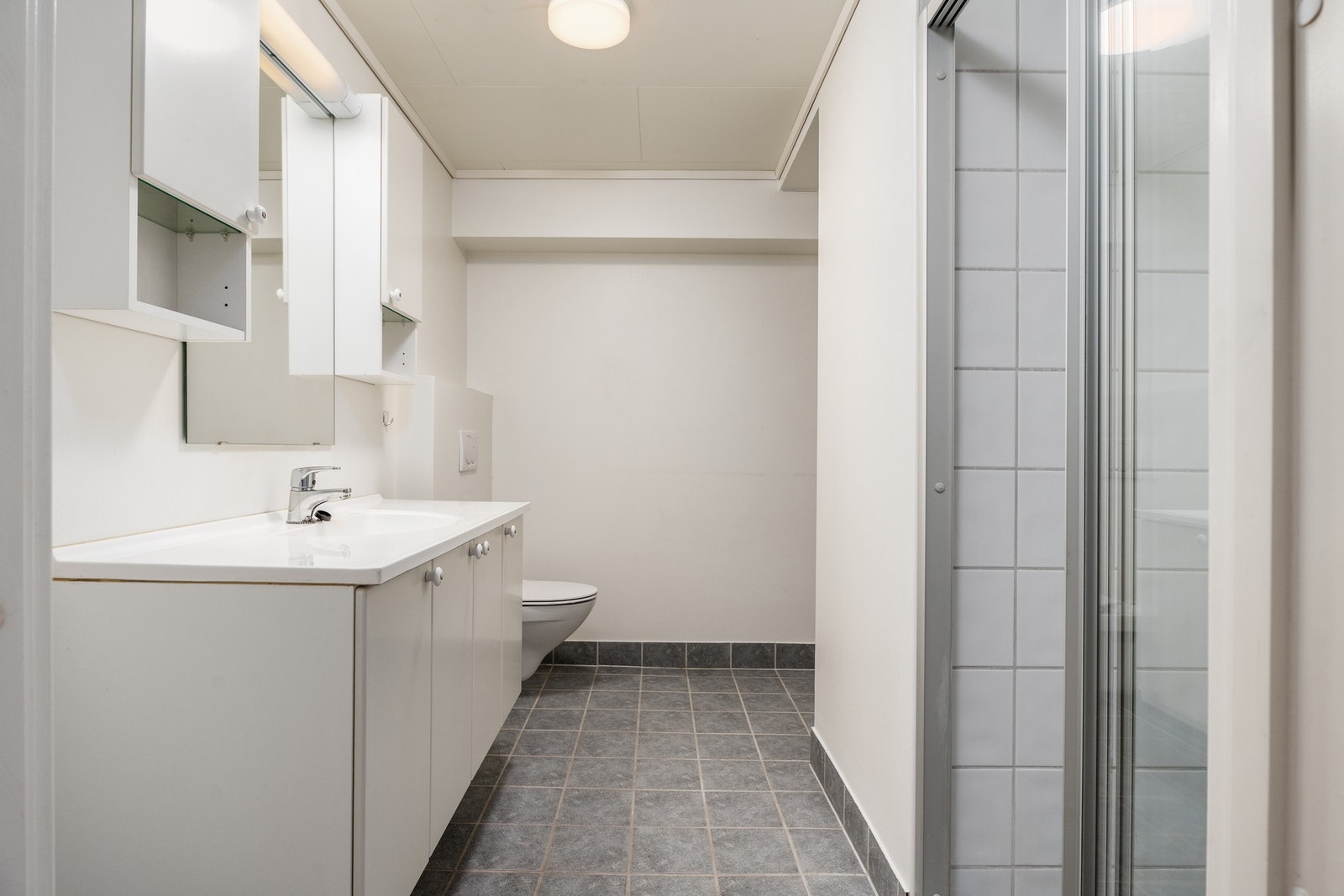 Lyst baderom med flislagt gulv og fliser i dusj. Galleribilde