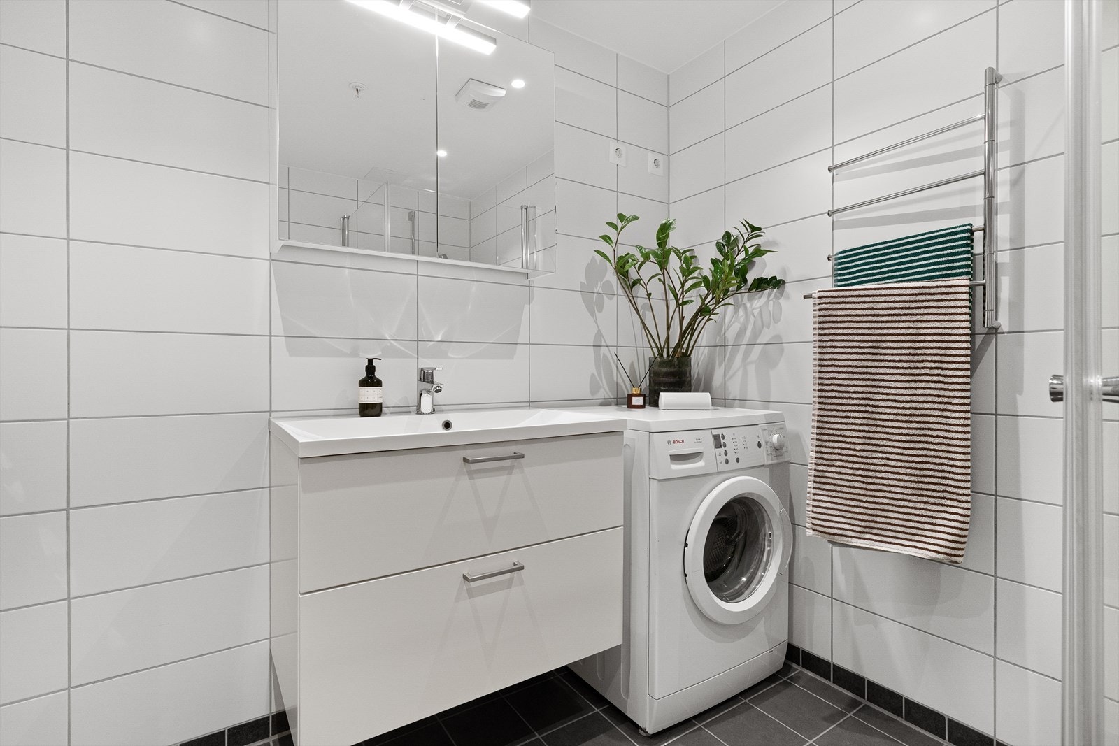 Badet er innredet med vegghengt toalett, dusjhjørne og moderne baderomsinnredning med speilskap Galleribilde