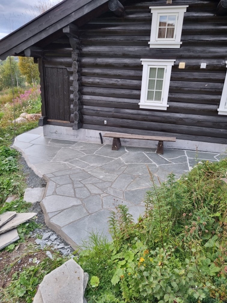 Skiferbelagt uteplass går langs hyttas langside og kortside, og forbindes med anneks og parkeringsplass via en natursteisntrapper Galleribilde
