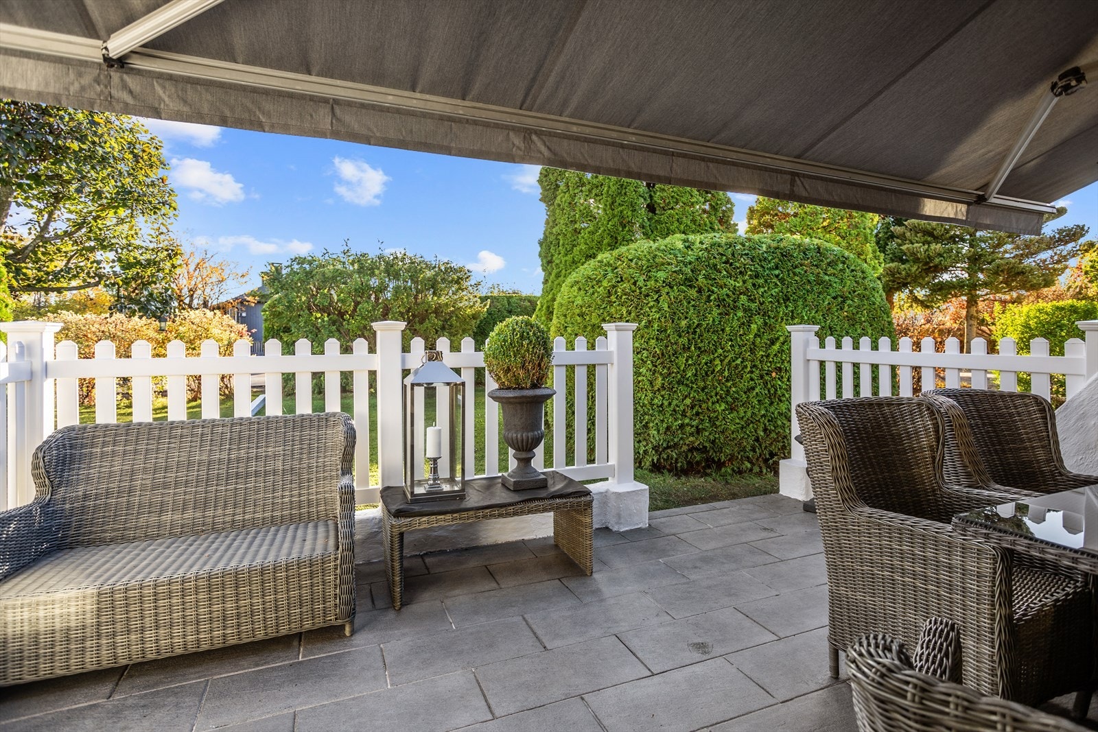 Terrassen er godt skjermet av murte sidevegg, gjerde og ikke minst av av planter og trær på tomten. Terrassemarkise dekker deler av uteplassen. Galleribilde