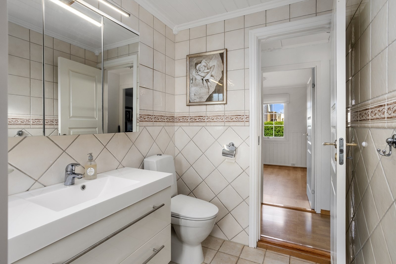 Baderomsinnredningen, med overliggende helstøpt servantbenk, har to brede kolonialskuffer med god oppbevaringsplass. Over denne er det 3-dørs speilskap med LED-bar. Ytterst på badet er det sokkeltoalett. Galleribilde