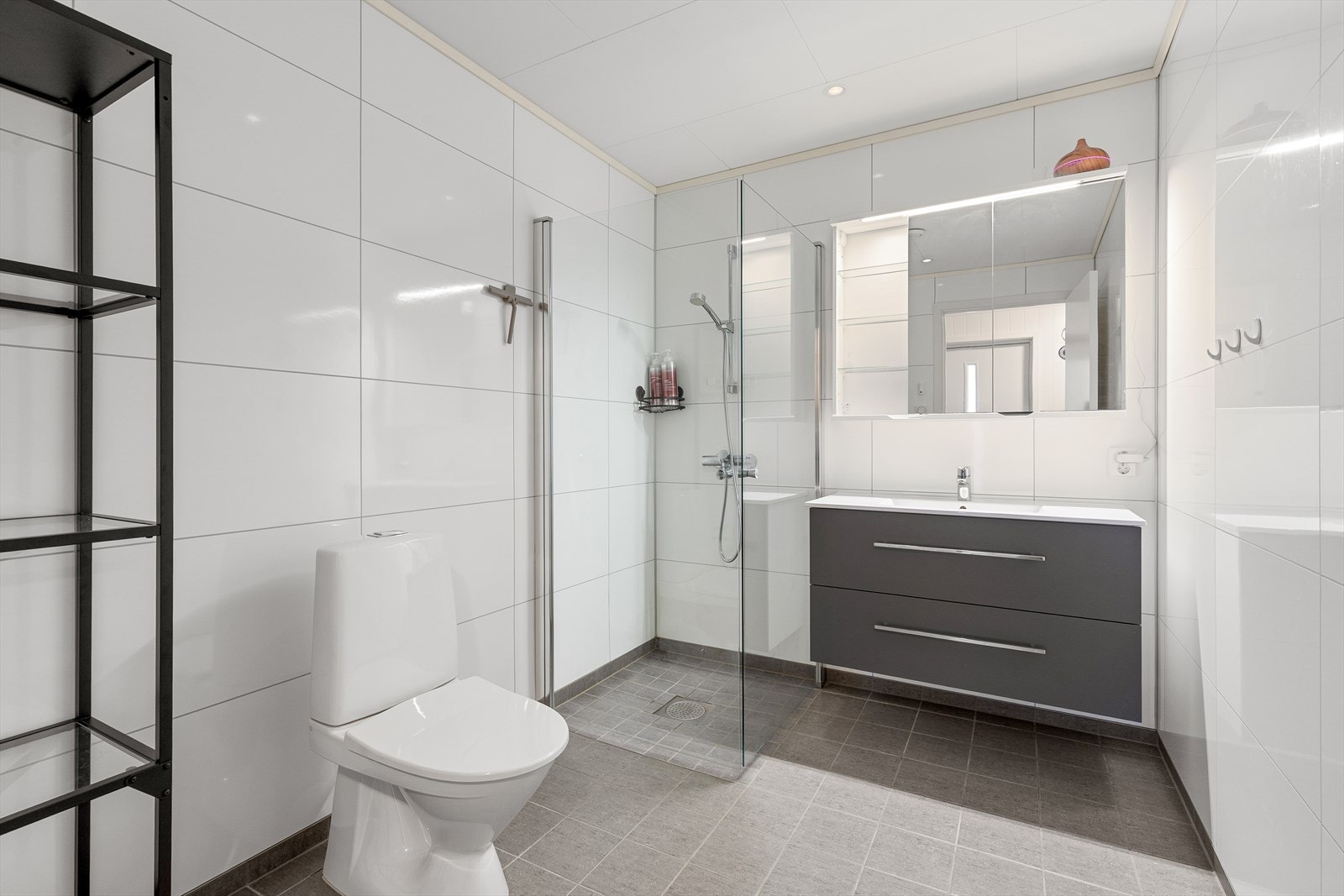 Baderommet har flislagt golv og baderomsplater på vegg Galleribilde