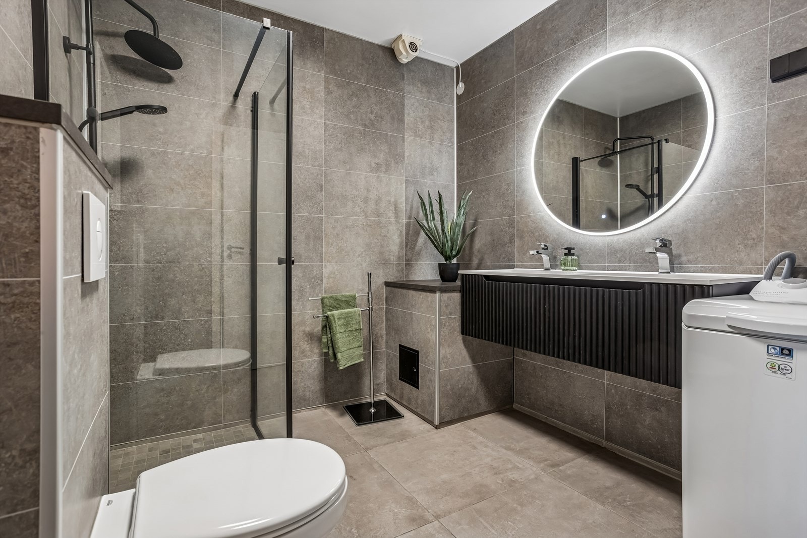 Et delikat bad med store fliser på gulvet og våtromsplater på veggene. Utstyrt med vegghengt toalett, moderne dobbeltservant med skuffeseksjon og speil med egen belysning. Pusset opp i 2023. Galleribilde