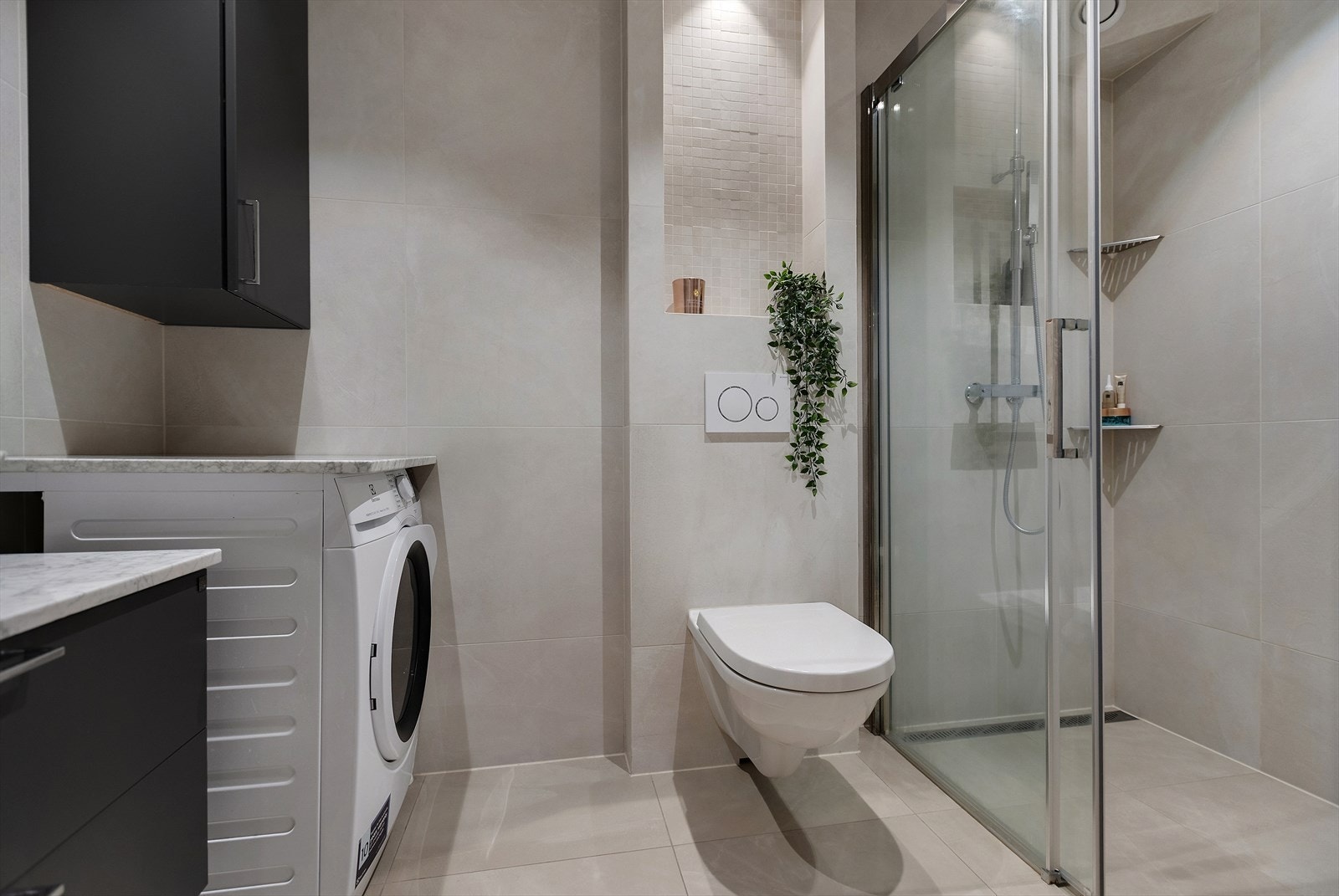 Badet er moderne og delikat med veggmontert WC, dusjplass med dusjvegger samt servant med ettgreps blandebatteri og tilhørende innredning. Galleribilde