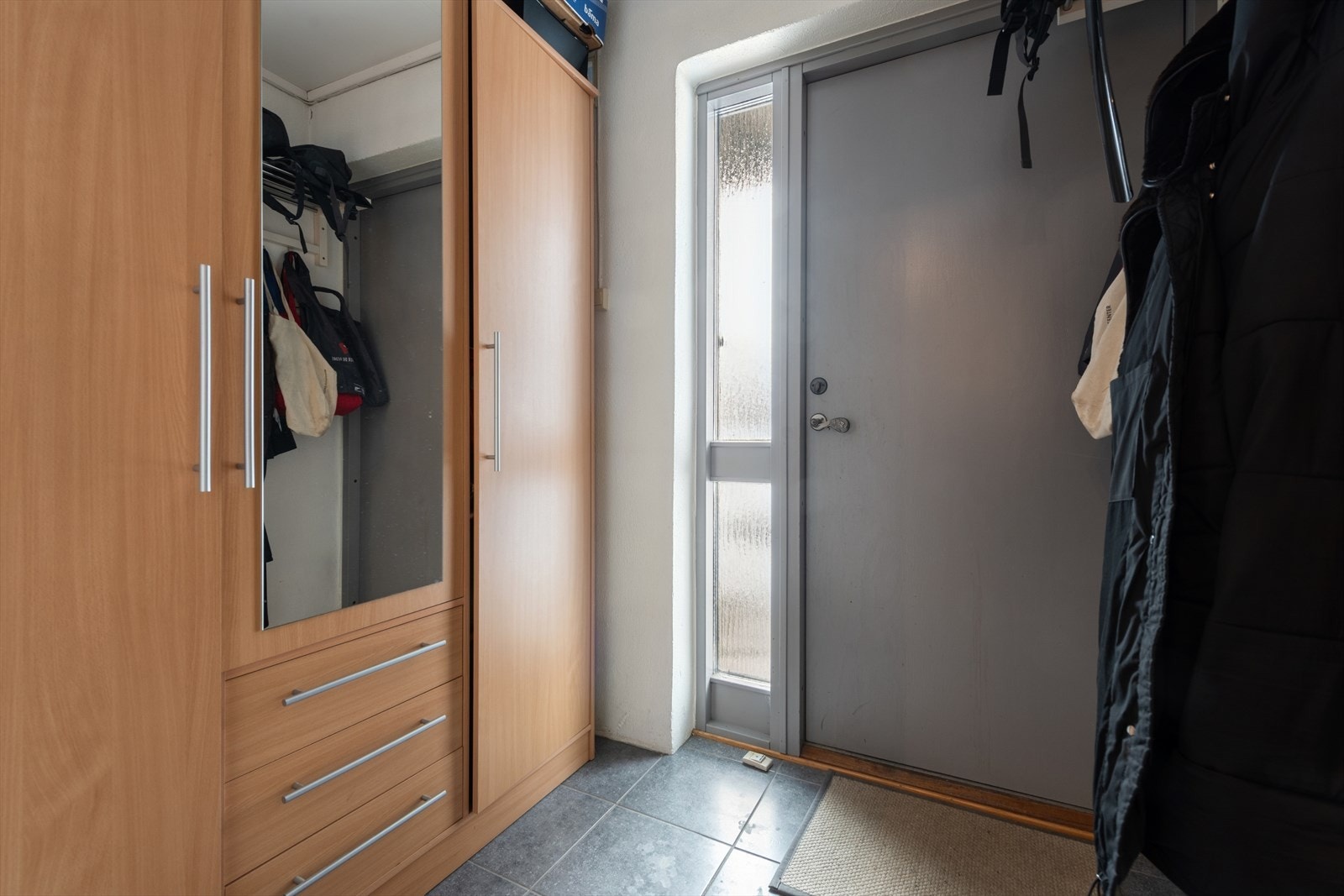 Entré/vindfang med fliser på gulv, knaggrekke og garderobeskap Galleribilde