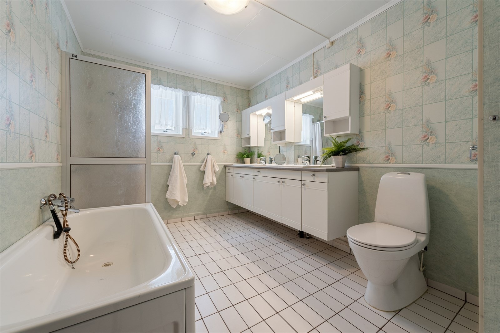 Stort bad med fliser på gulv med underliggende varme. Badet er videre utstyrt med badekar, dusjkabinett, dobbeltservant og wc Galleribilde