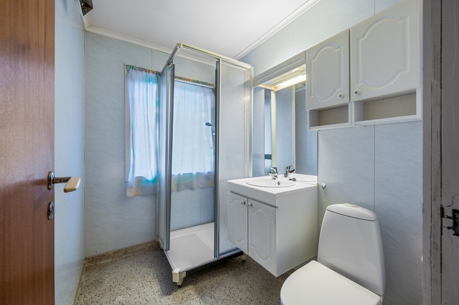 Badet måler 3,5 m² og inneholder toalett, helstøpt servant, skap under servant med profilerte fronter og dusjkabinett. Galleribilde