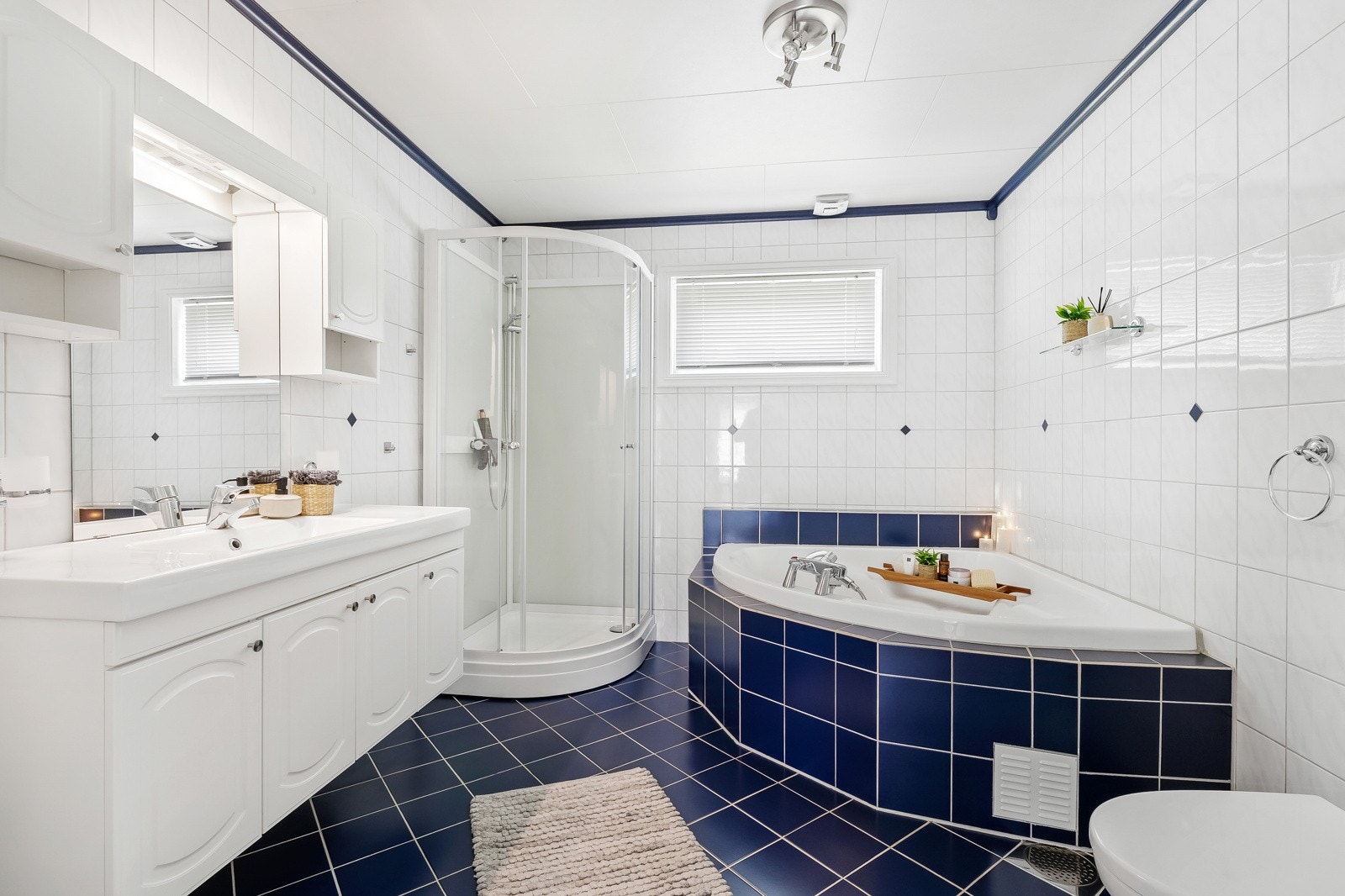 Flislagt bad med dusjkabinett, baderomsinnredning med speil, toalett og badekar. Galleribilde