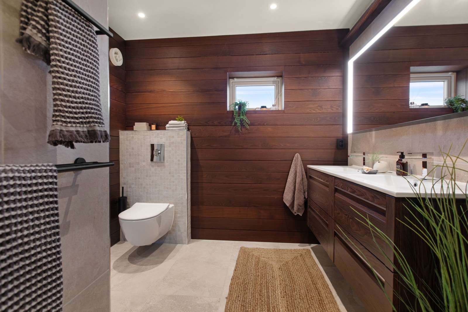 Badet er utstyrt med speil med belysning, et vegghengt toalett og en nedsenket dusjnisje med skyvedør i glass. Galleribilde