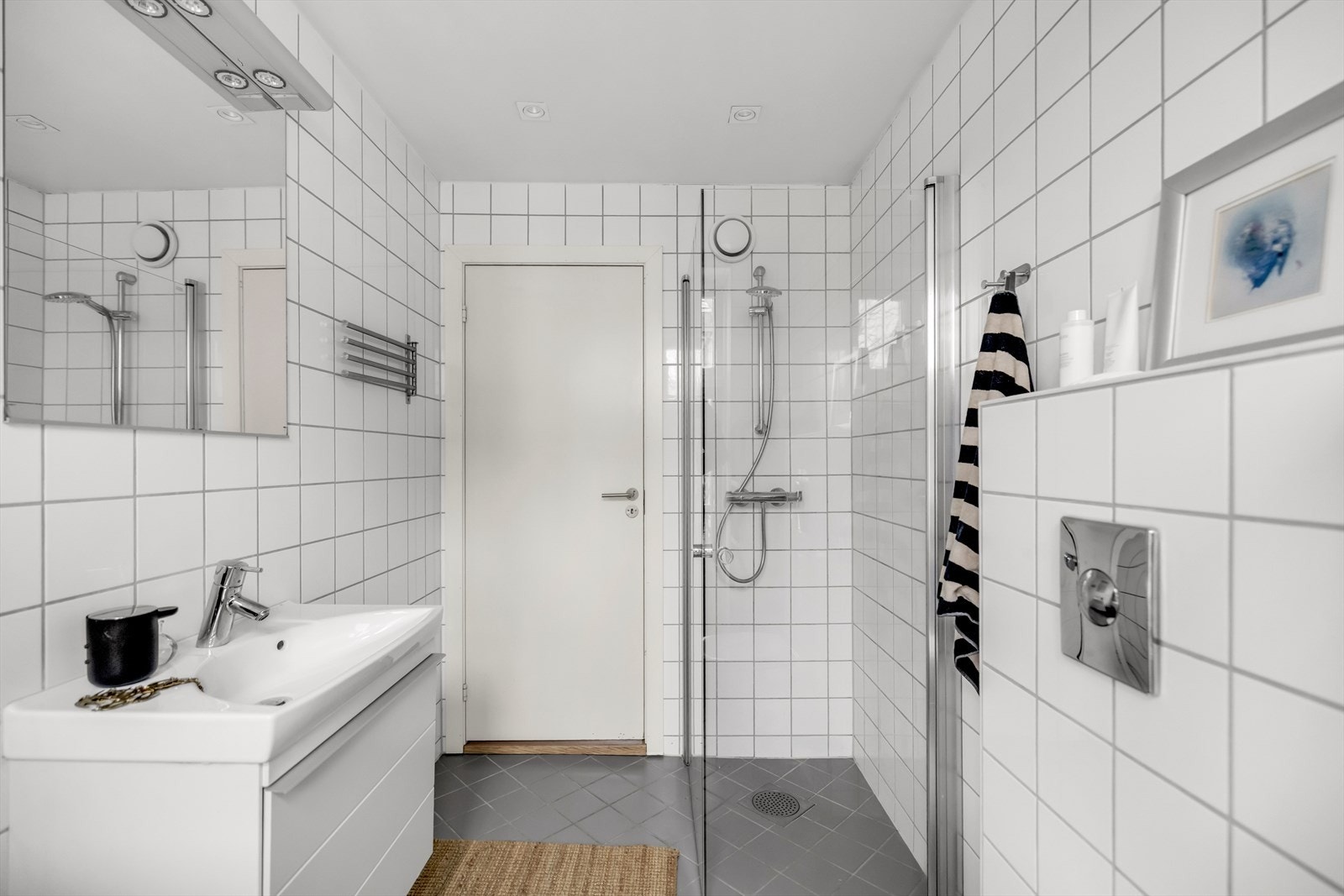 Badet er innredet med vegghengt klosett, servant nedfelt i innredning, speil med lys og dusjhjørne med svingbare glassdører. Det er også opplegg for vaskemaskin. Galleribilde