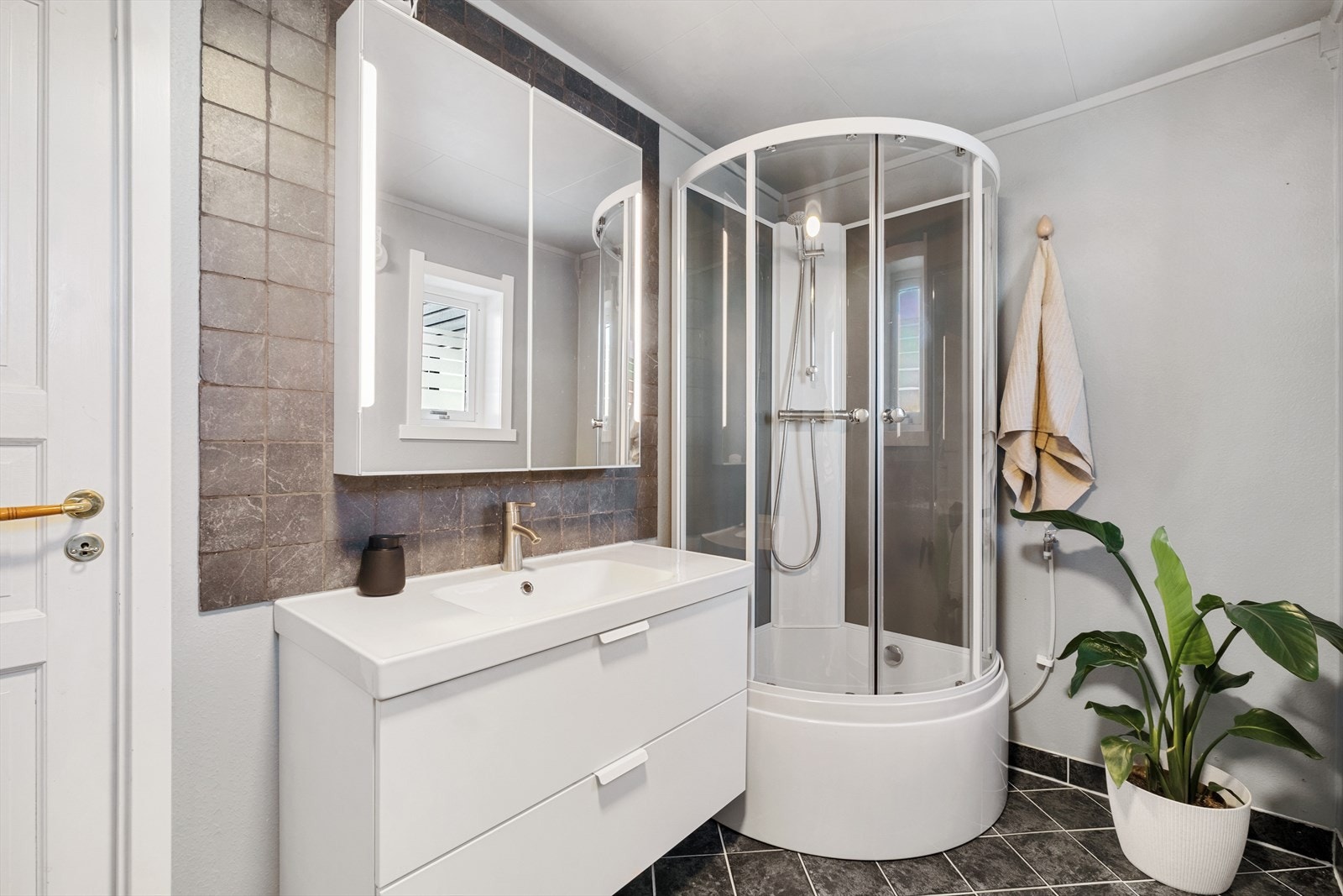 Badet er innredet med et vegghengt toalett, en servant nedfelt i baderomsinnredningen og et dusjkabinett. Galleribilde