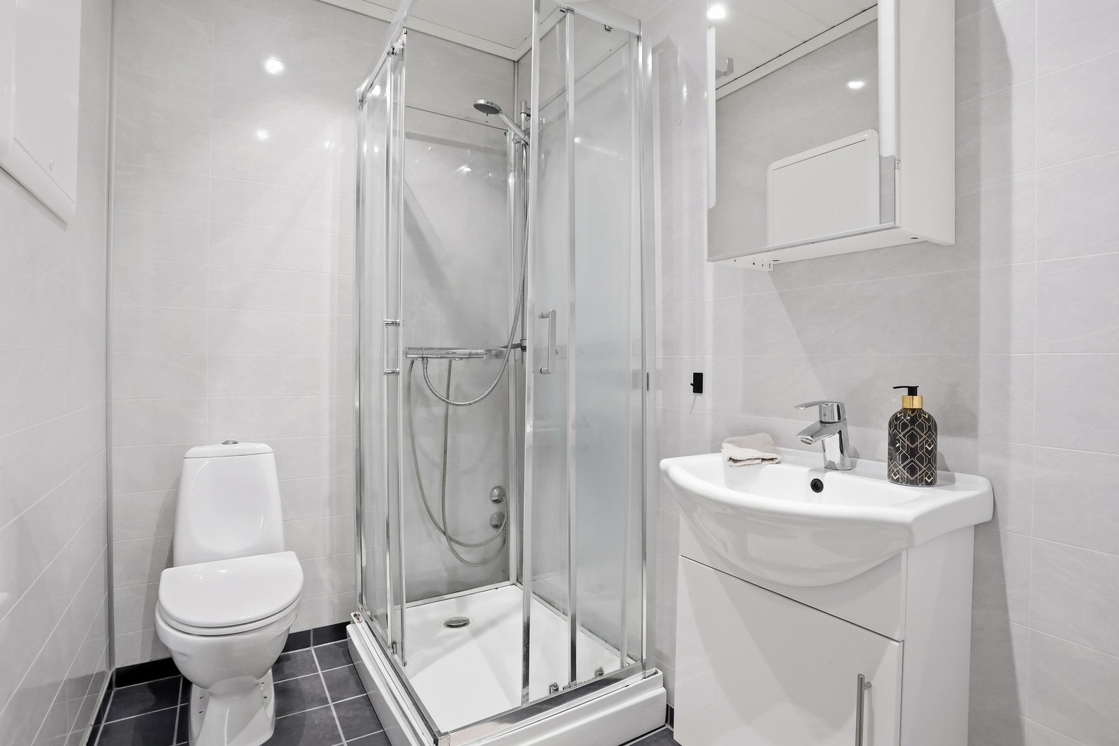 Pent baderom fra ca. 2020 med servant, toalett, dusjkabinett og opplegg for vaskemaskin. Galleribilde