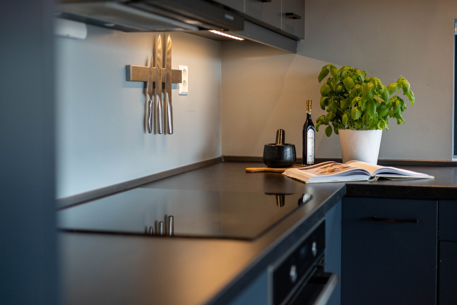 Gjennomført stil med mørk benkeplate, sorte detaljer og praktisk belysning under overskapene Galleribilde