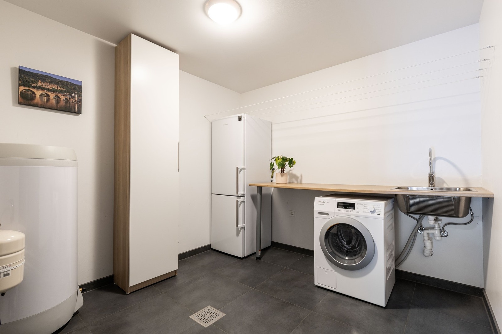 Et romslig og praktisk vaskerom med mørke gulvfliser som tåler daglig bruk Galleribilde