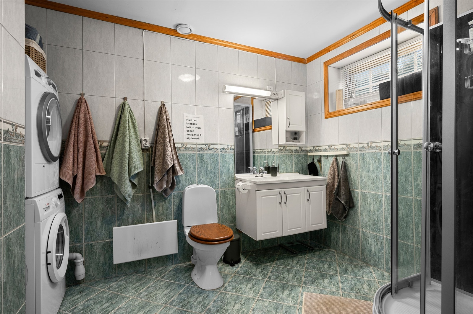 Romslig bad på 7 kvm med flislagte flater, opplegg for vaskemaskin og trommel, servantskap med speil og lys, toalett og dusjhjørne. Galleribilde