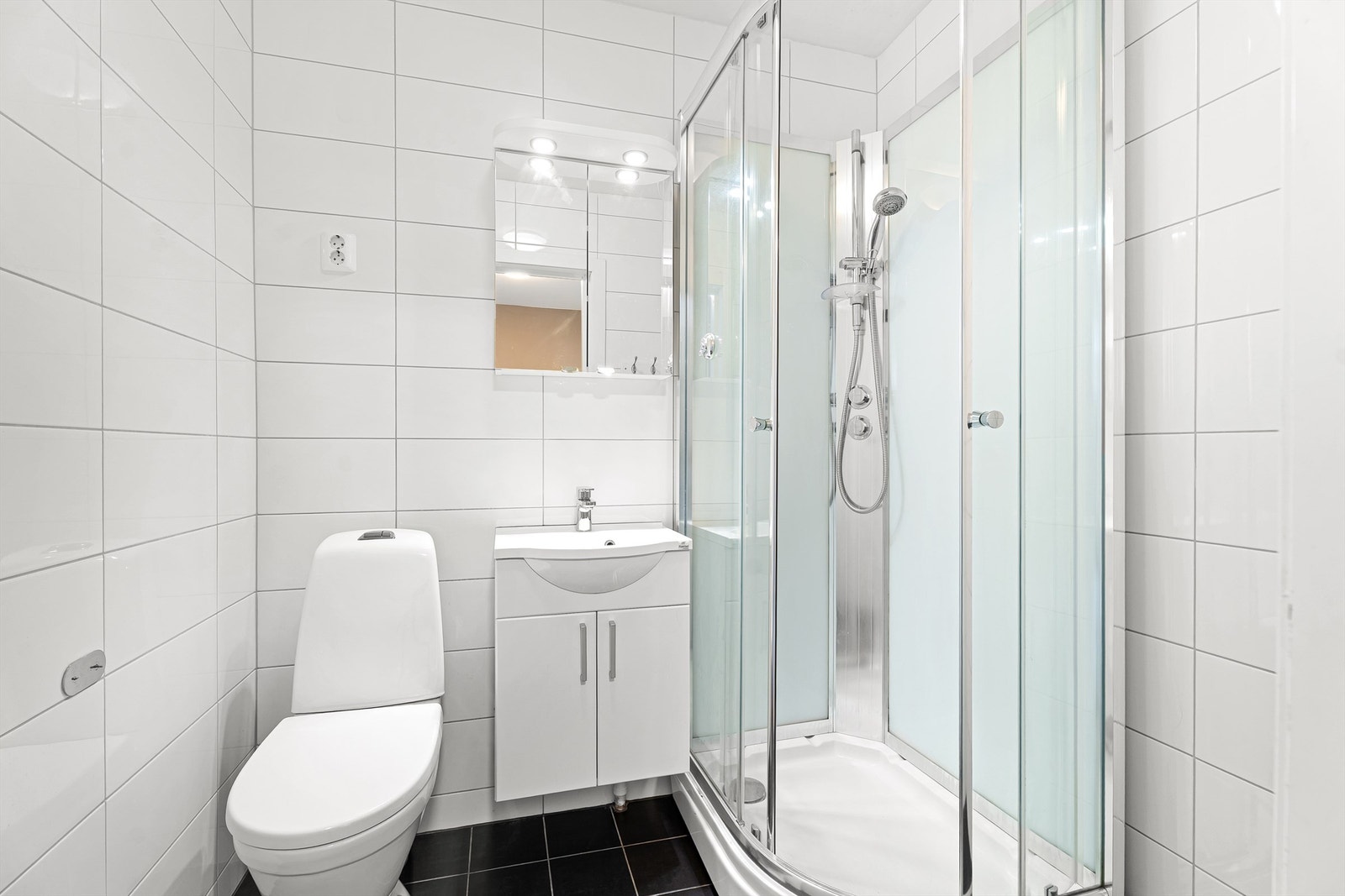 Badet har fliser på gulv med gulvvarme, dusjkabinett, servant med oppbevaring samt toalett. Galleribilde