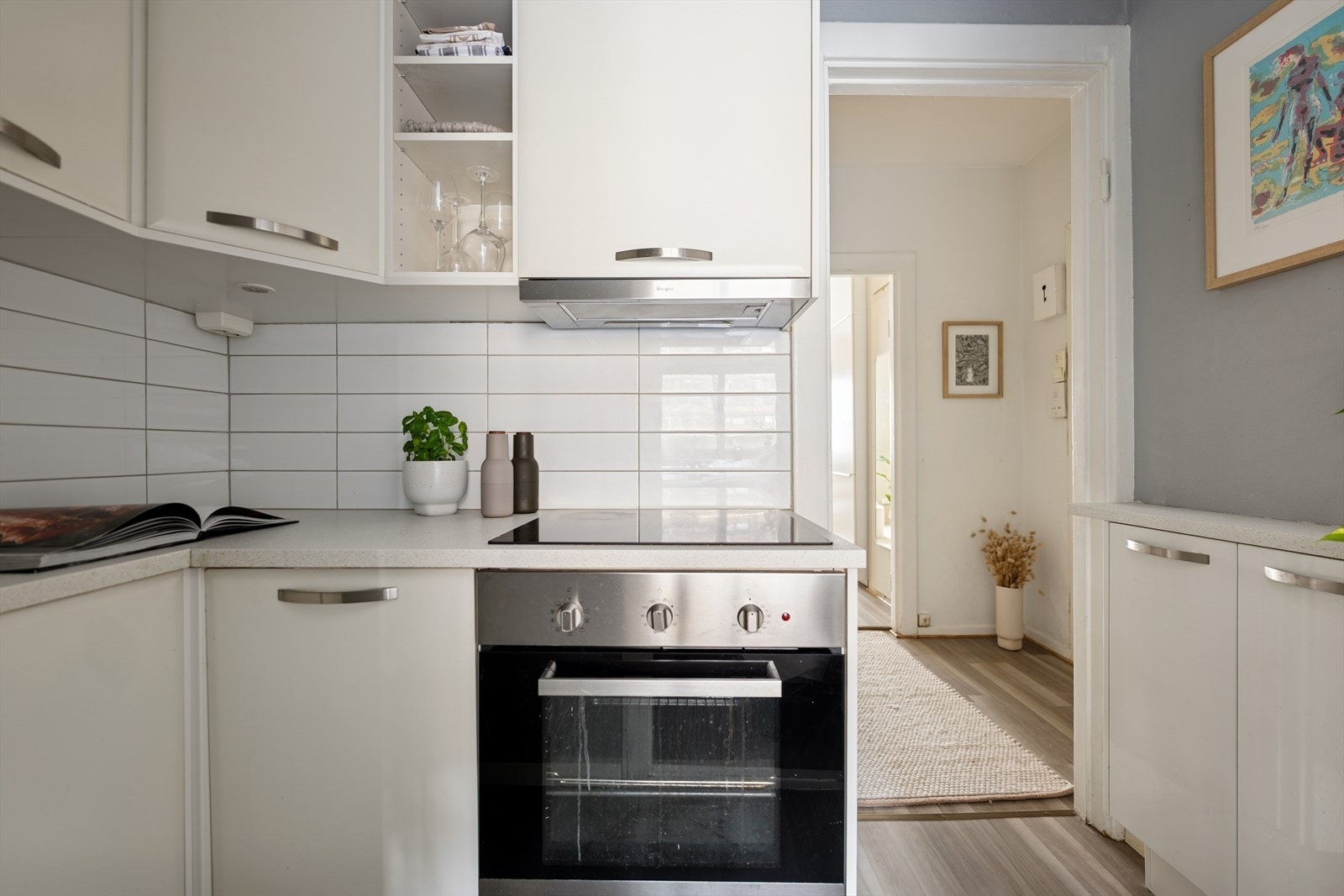 Kjøkkeninnredningen fra IKEA har glatte hvite fronter, laminert benkeplate, flislagt backsplash, integrert oppvaskmaskin, stekeovn og induksjonstopp. Innredningen ble montert i 2015. Galleribilde