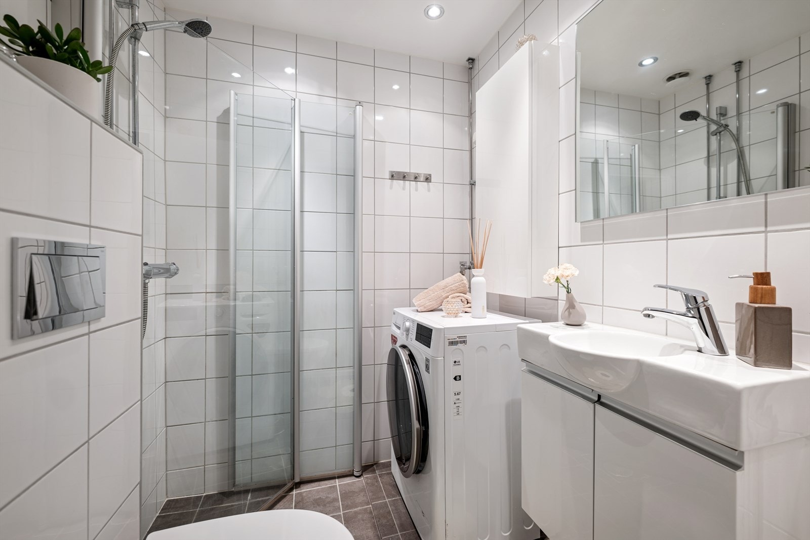 Lyst og flislagt bad fra 2013 med varmekabler i gulv, vegghengt klosett, dusjhjørne, servant med underskap og opplegg for vaskemaskin. Galleribilde