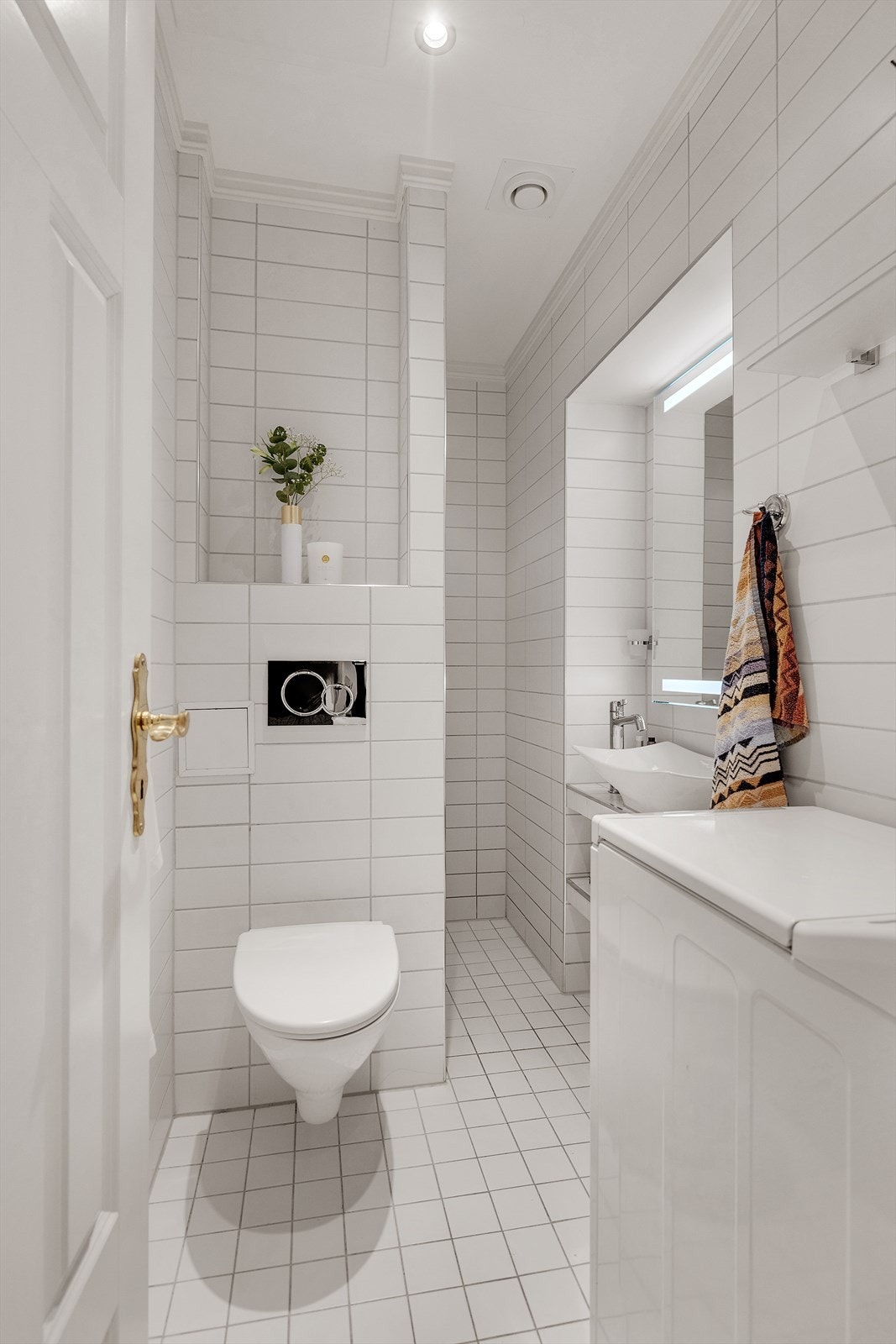 Baderommet er flislagt og har downlights i himling, og består av vegghengt toalett, servant med oppbevaring i hyller, speil med integrerte lys, dusjsone og opplegg for liten vaskemaskin. Galleribilde