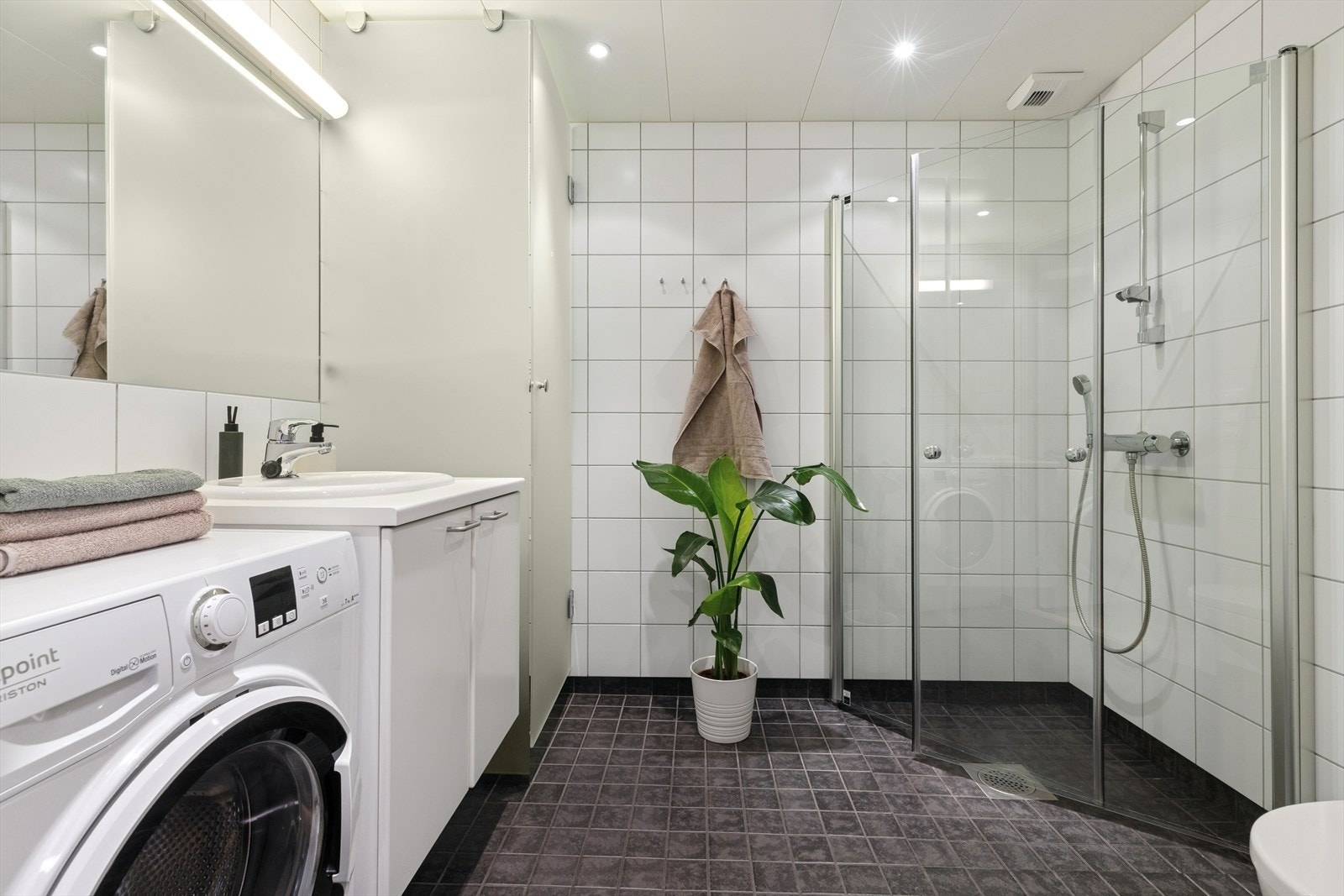 Badet er utstyrt med åpen dusj med dusjvegger, vegghengt toalett og skapinnredning med nedfelt porselensservant, speil og god oppbevaringsplass. Galleribilde