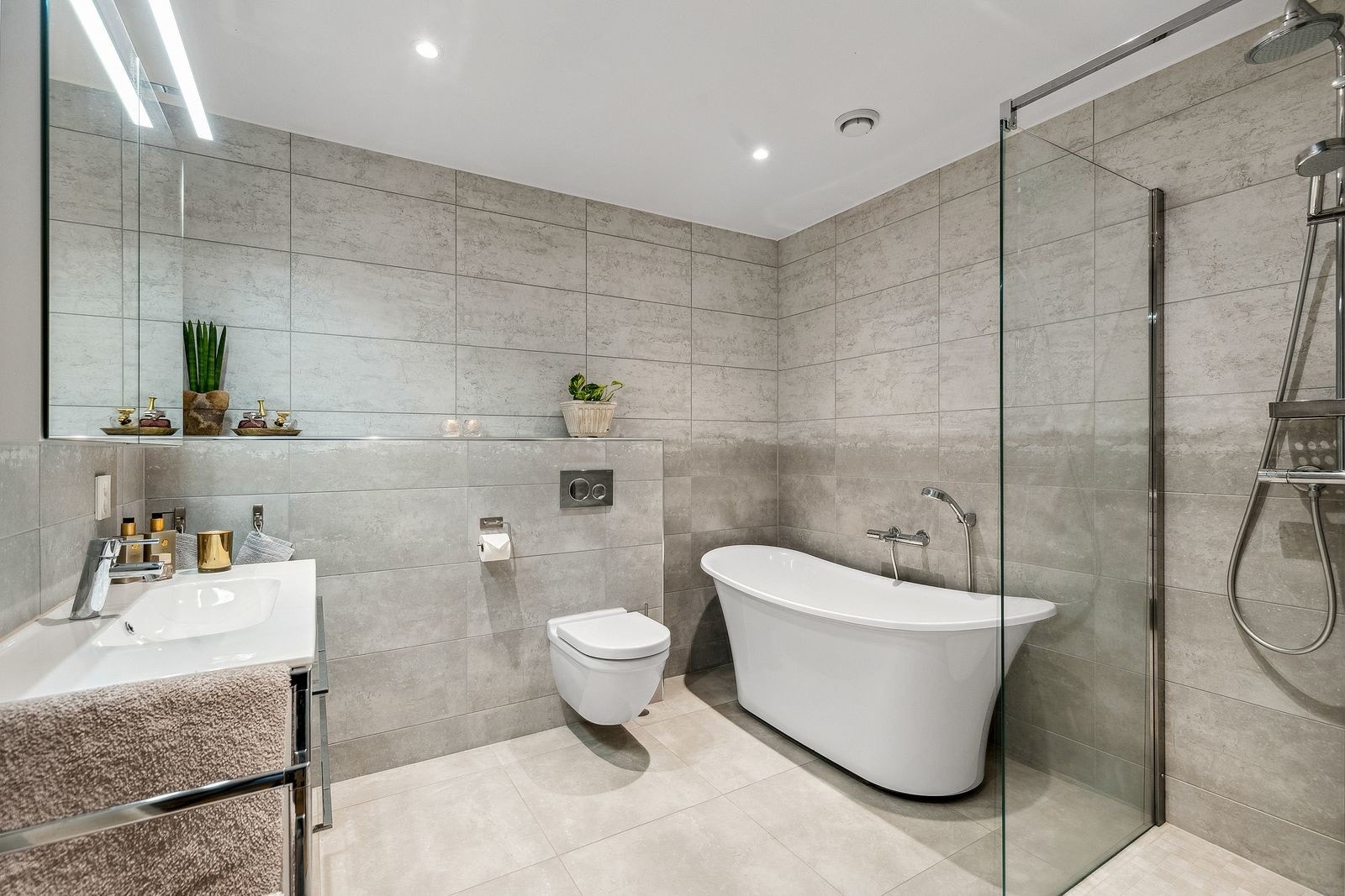 Lekkert baderom i første etasje med fliser, varmekabler og downlights. Rommet er innredet med vegghengt toalett, dusjhjørne med glassvegg, frittstående badekar og servant med underskap og speilskap. Galleribilde