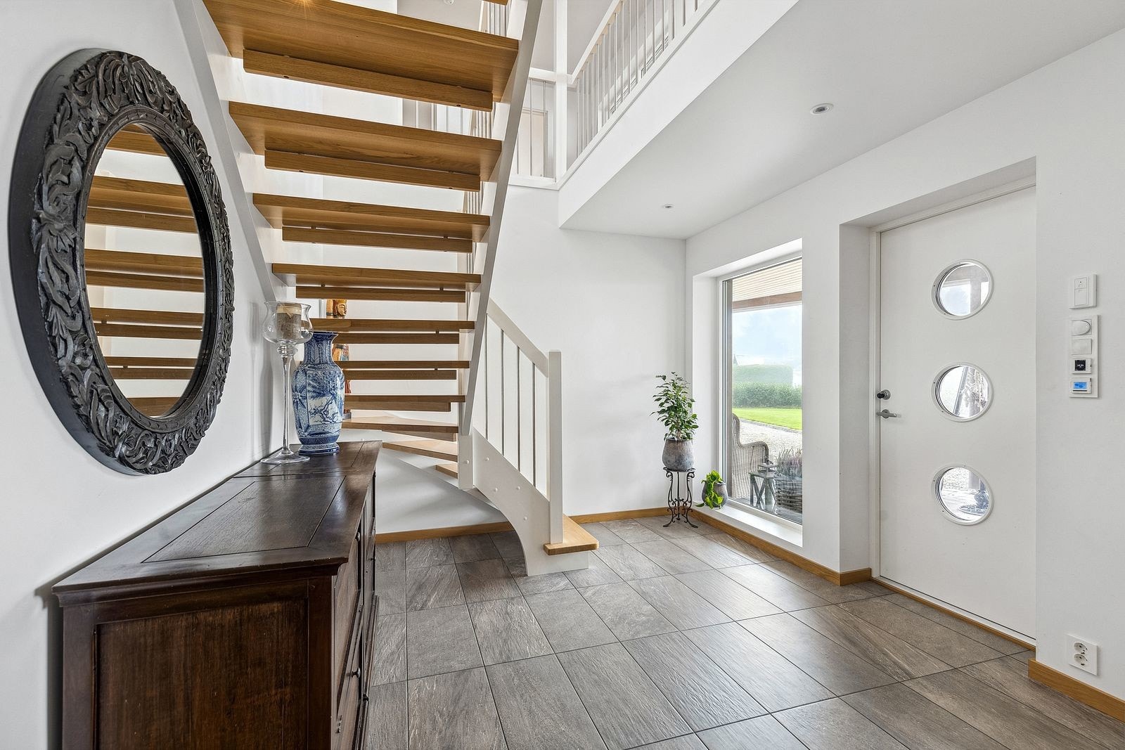 Lys og romslig entré med flislagt gulv, behagelig gulvvarme og store vindusflater som slipper inn rikelig med dagslys. God plass til oppbevaring. Galleribilde