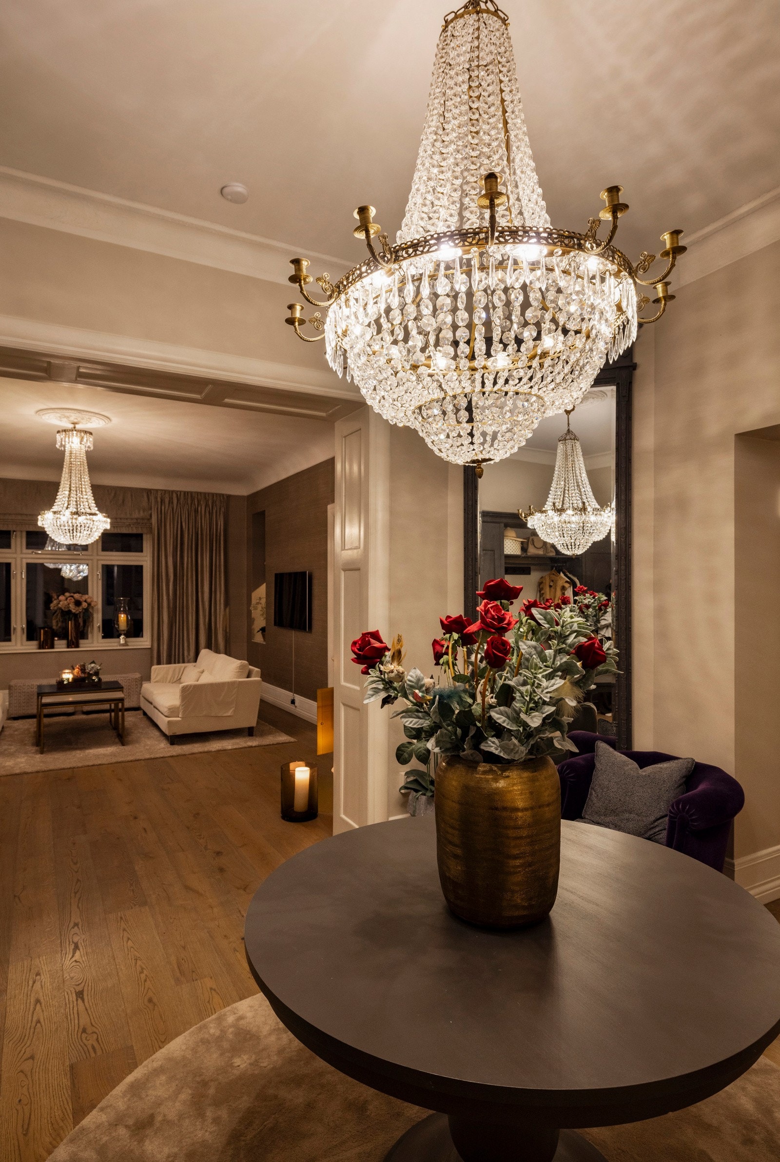 Den majestetiske lysekronen fyller rommet med varm glød og fremhever de brede døråpningene og detaljene rundt - diskret luksus i sitt rette element. Galleribilde